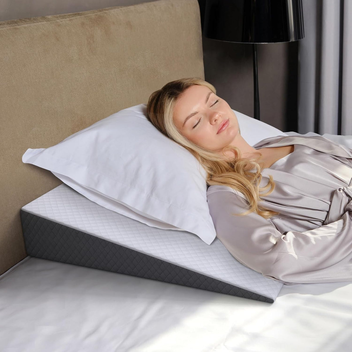 Close-up of wedge pillow corner and quilted side panel with a woman’s face and bedside lamp visible