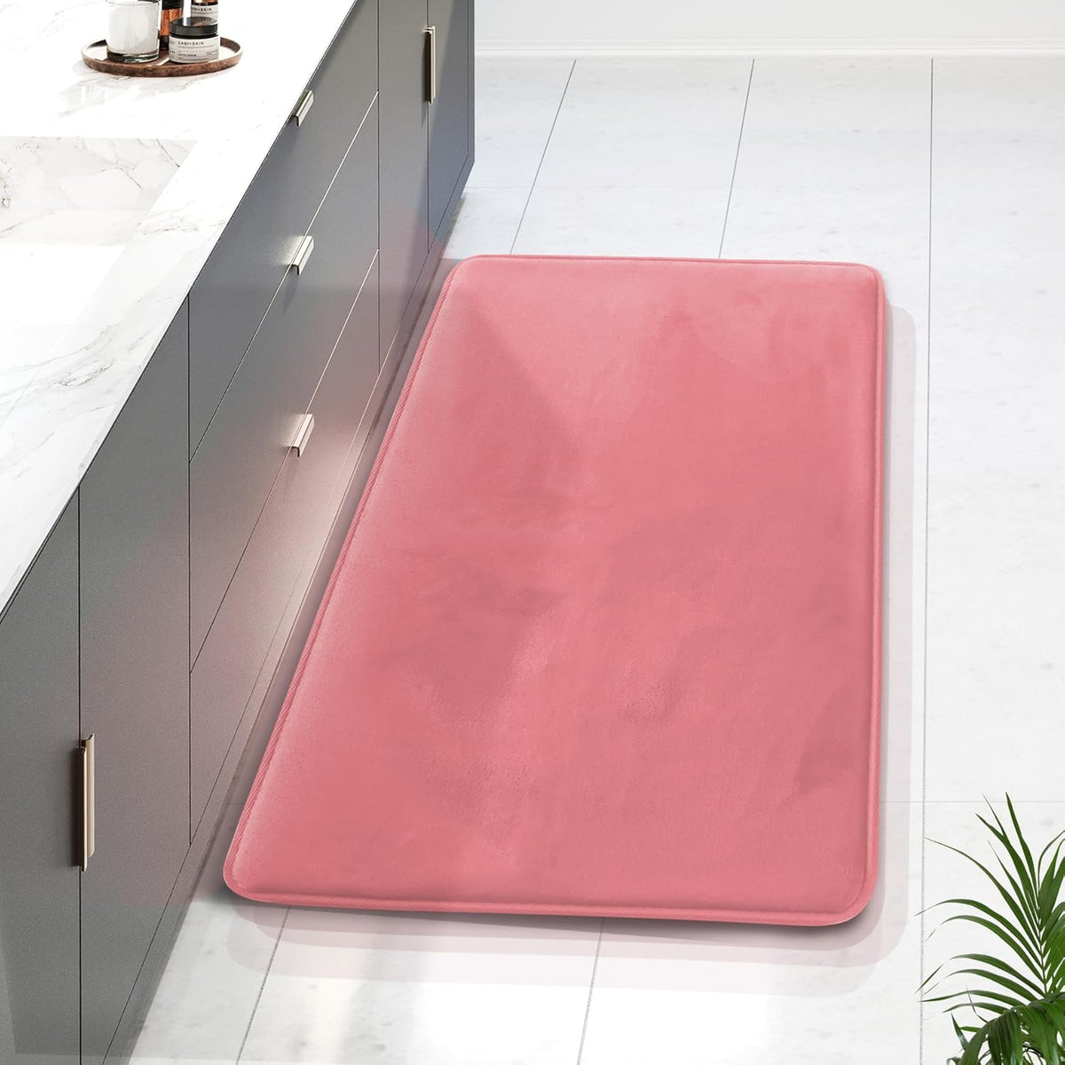 Top-down view of a single pink rectangular bath mat beside a dark gray vanity on white tile