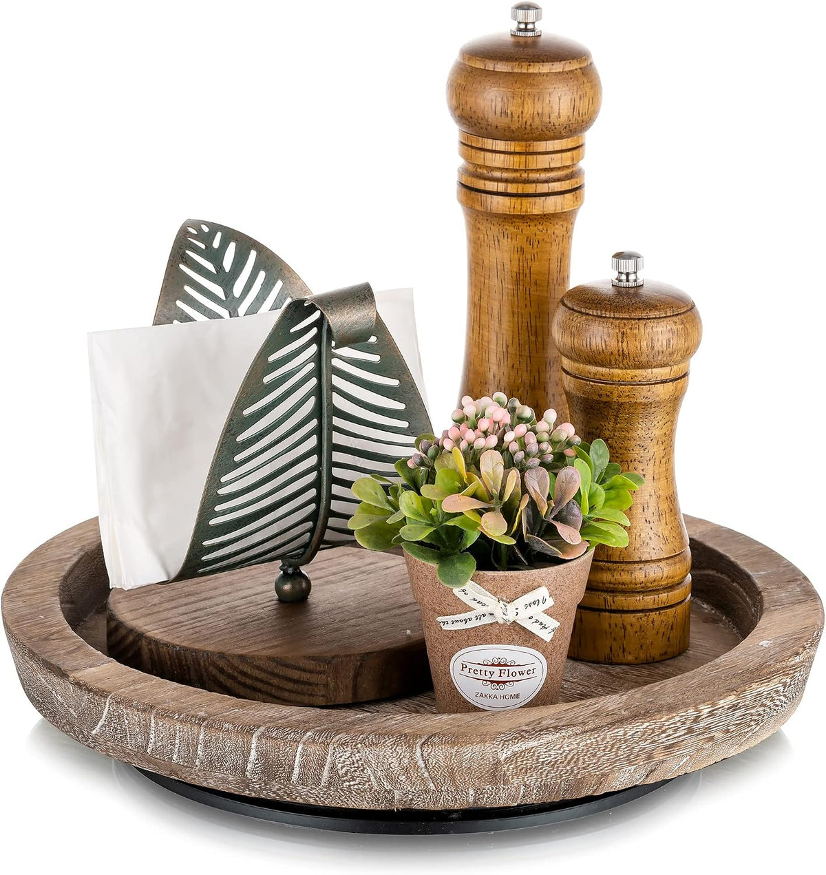 Dark brown round wooden tray holding pepper mills, napkin holder and a small potted faux plant