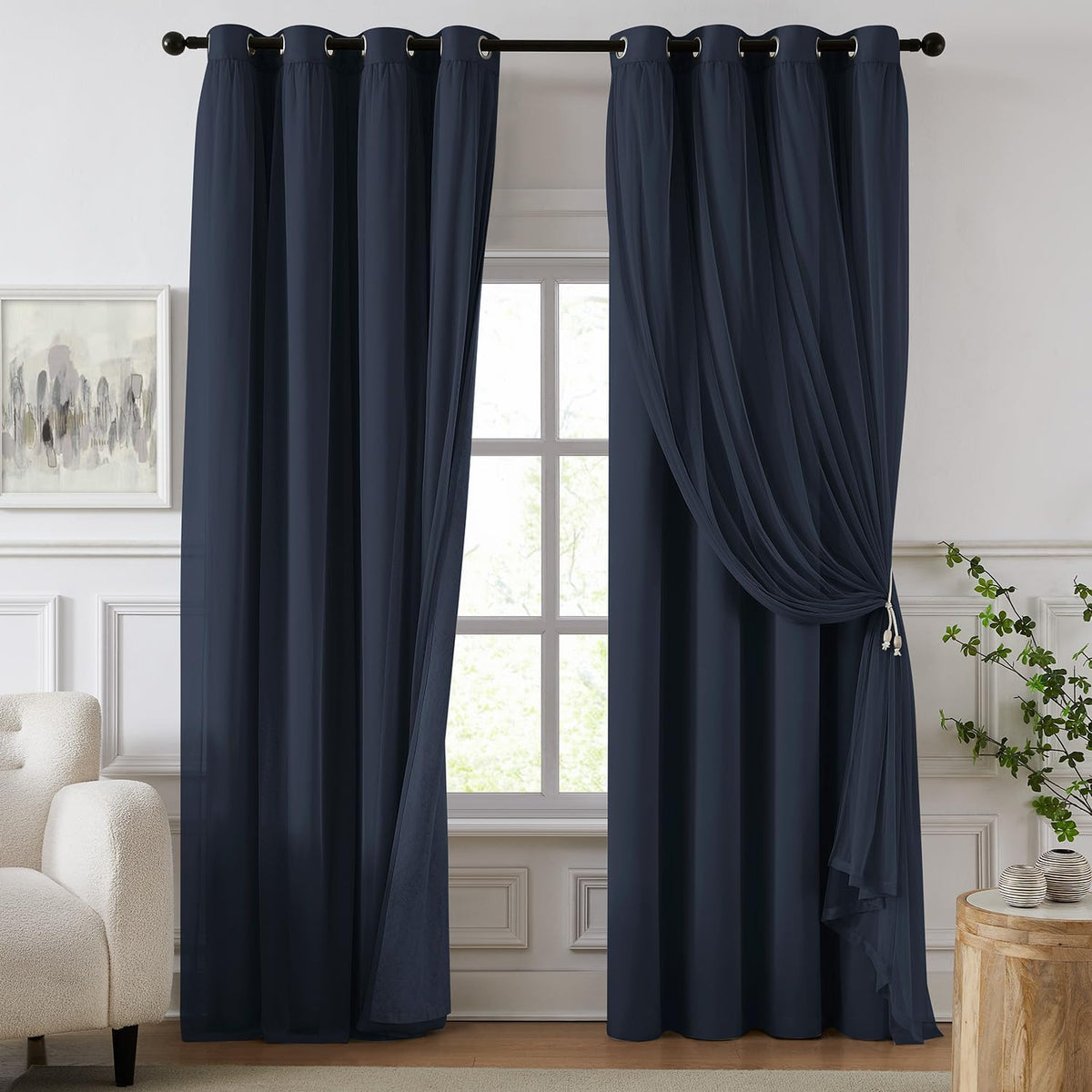 Navy blackout curtains with a sheer overlay gathered to one side framing a window in a styled room.