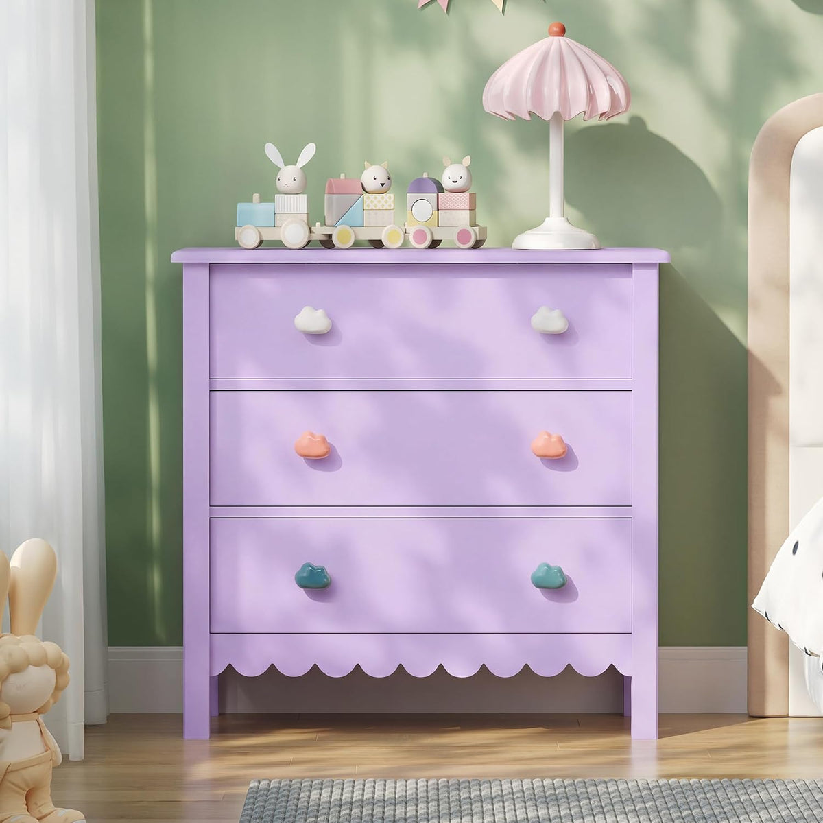 Front view of a purple scalloped three-drawer dresser with cloud-shaped knobs in a child's bedroom scene.