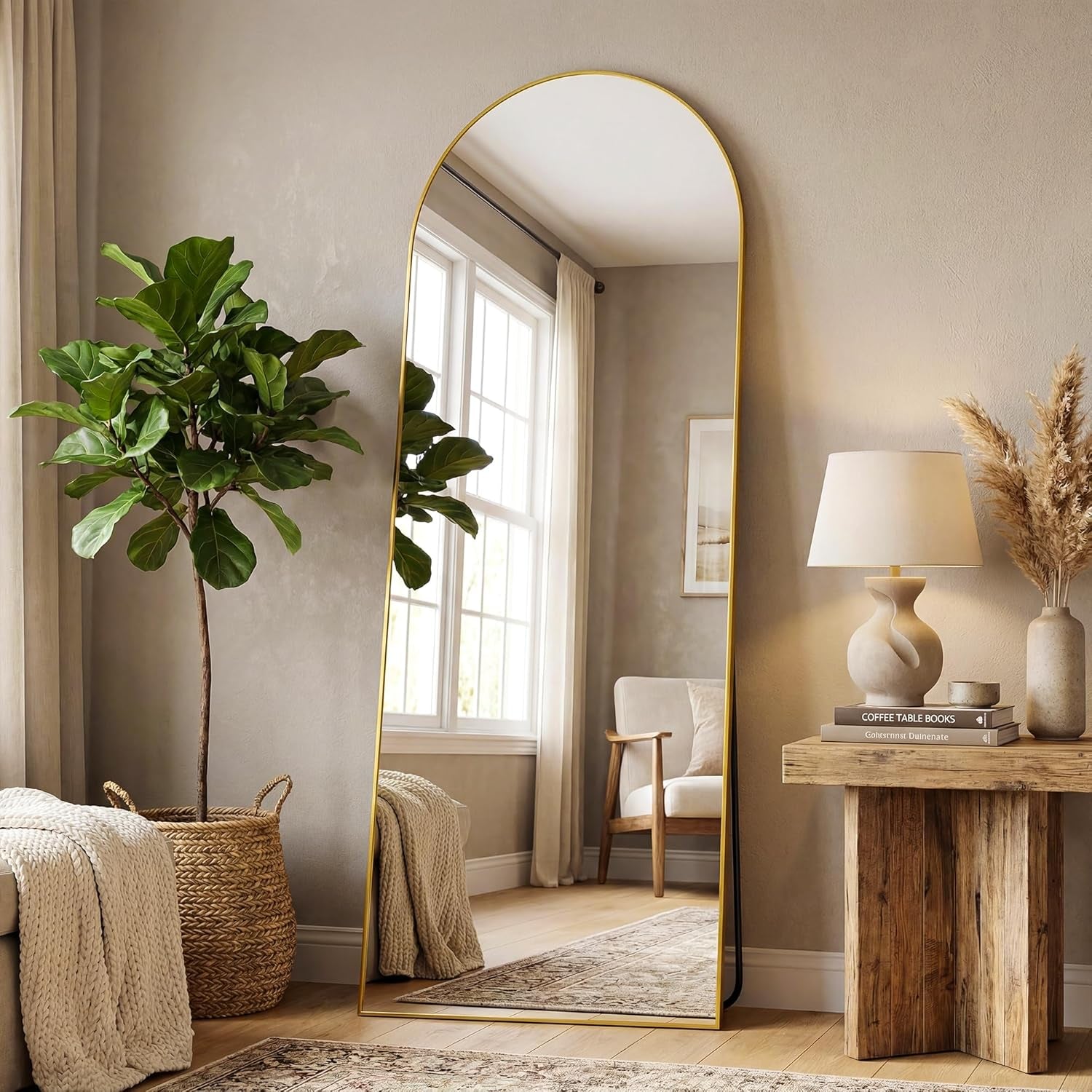 Arched floor mirror with a slim gold frame standing next to a potted plant and wooden side table.
