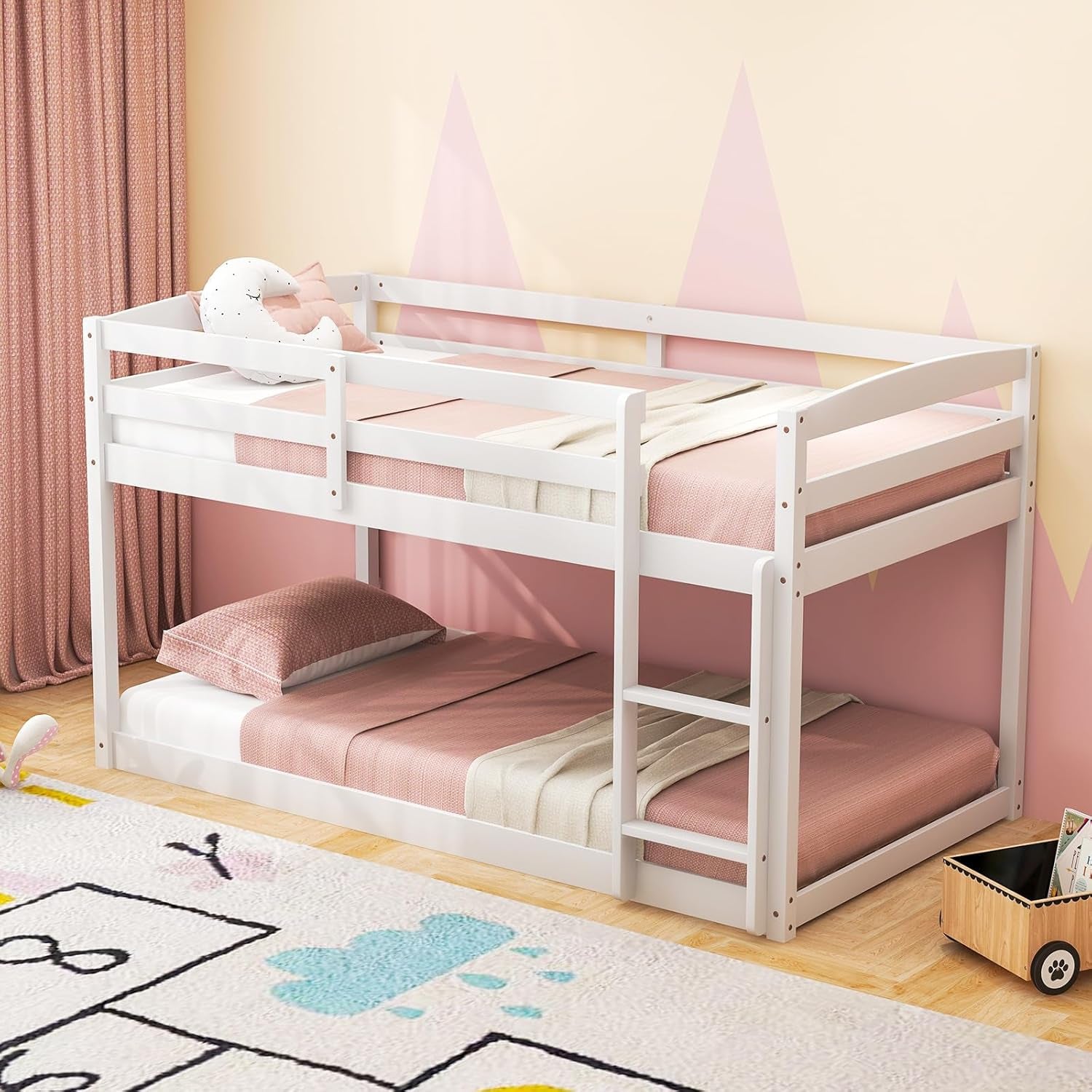 White twin-over-twin low bunk bed in a pink-themed kids' room with ladder on the right.