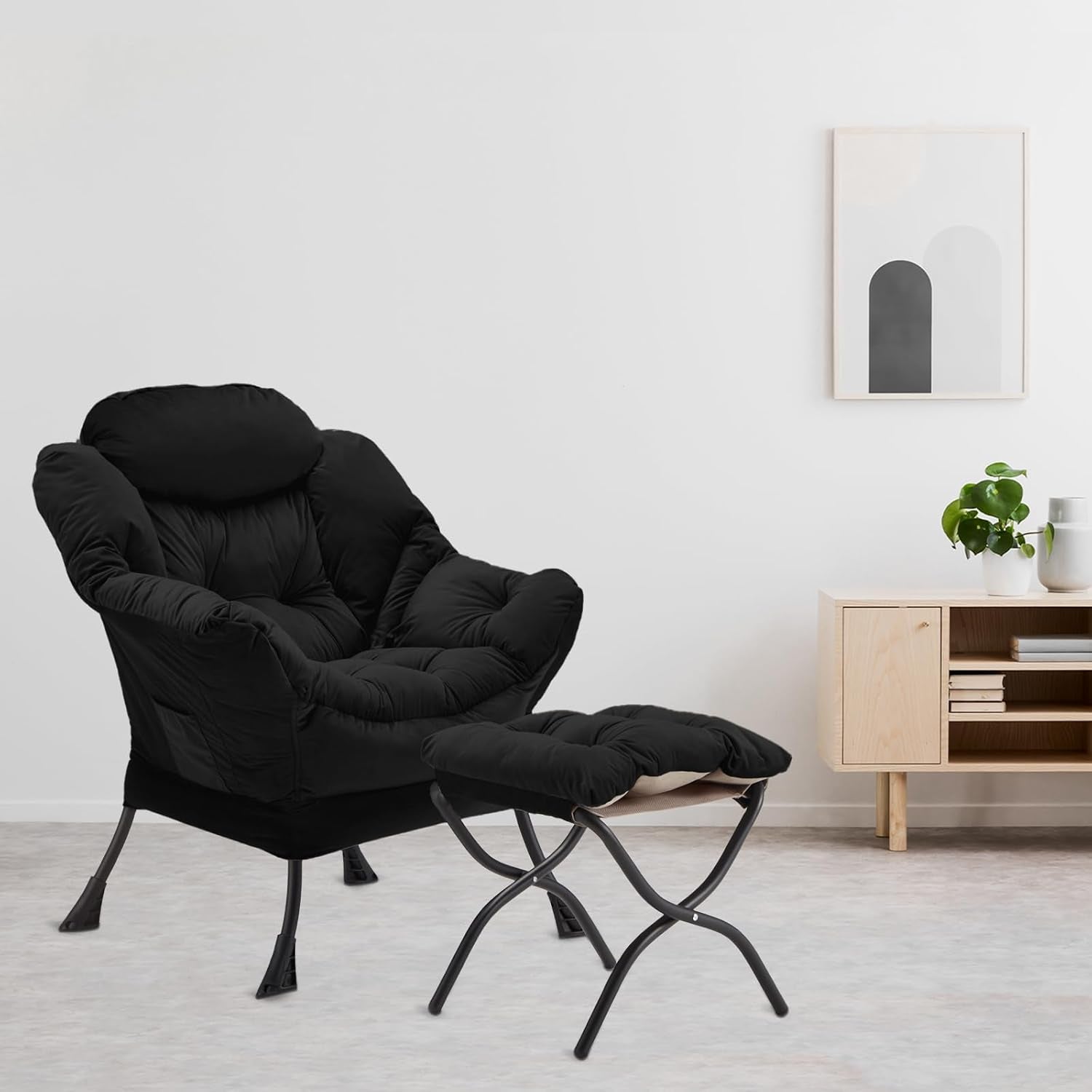 Black padded lounge chair with matching folding ottoman in a minimal room beside a light wood cabinet.