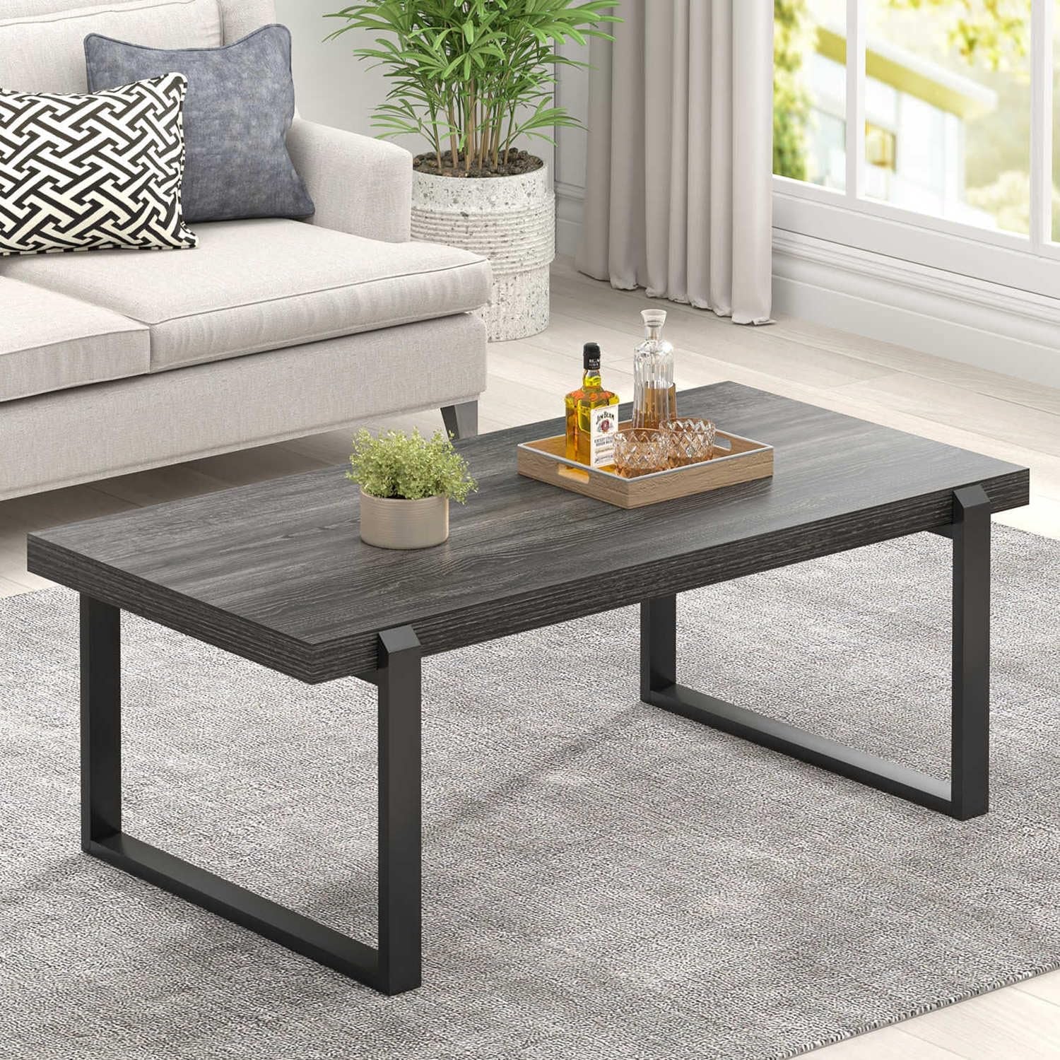 Low-angle view of a dark charcoal wood-grain coffee table with black U-shaped legs, tray and small plant on top.