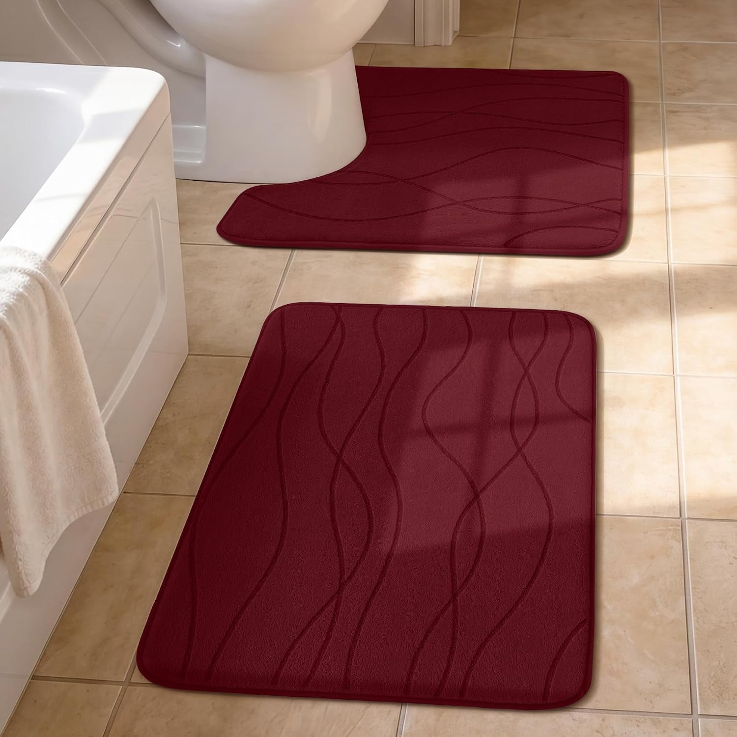 Close view of two burgundy bath mats on tiled floor near a bathtub and toilet.