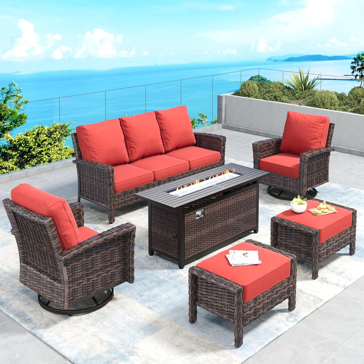 Outdoor wicker seating set with red cushions, ottomans and a rectangular fire pit table on a terrace.