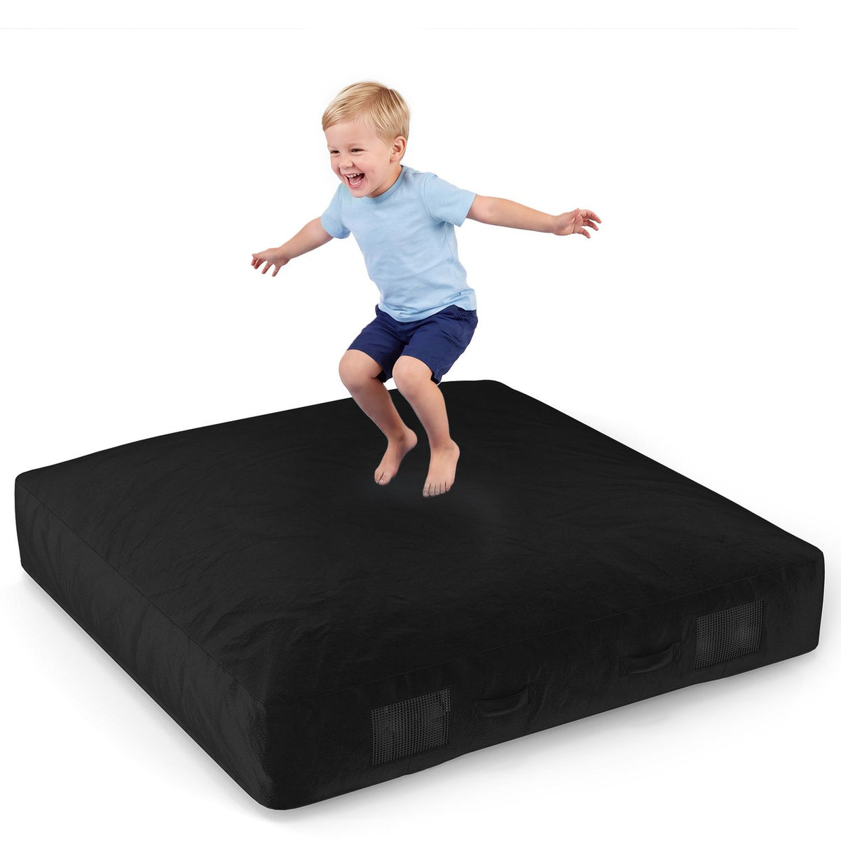 A child jumps on a black crash pad against a white background.