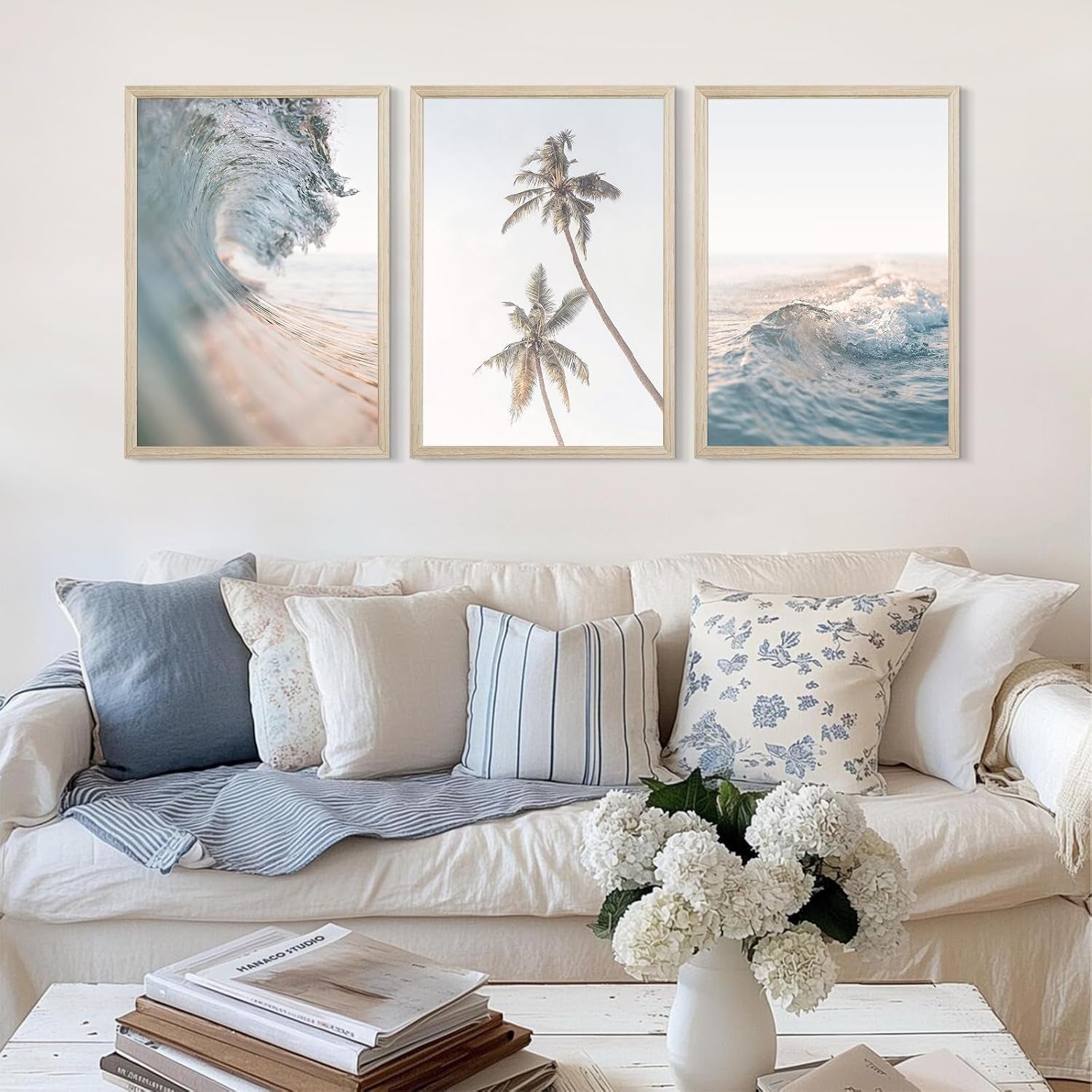 Three framed beach prints hung above a cream sofa with patterned and striped throw pillows and a coffee table with books and