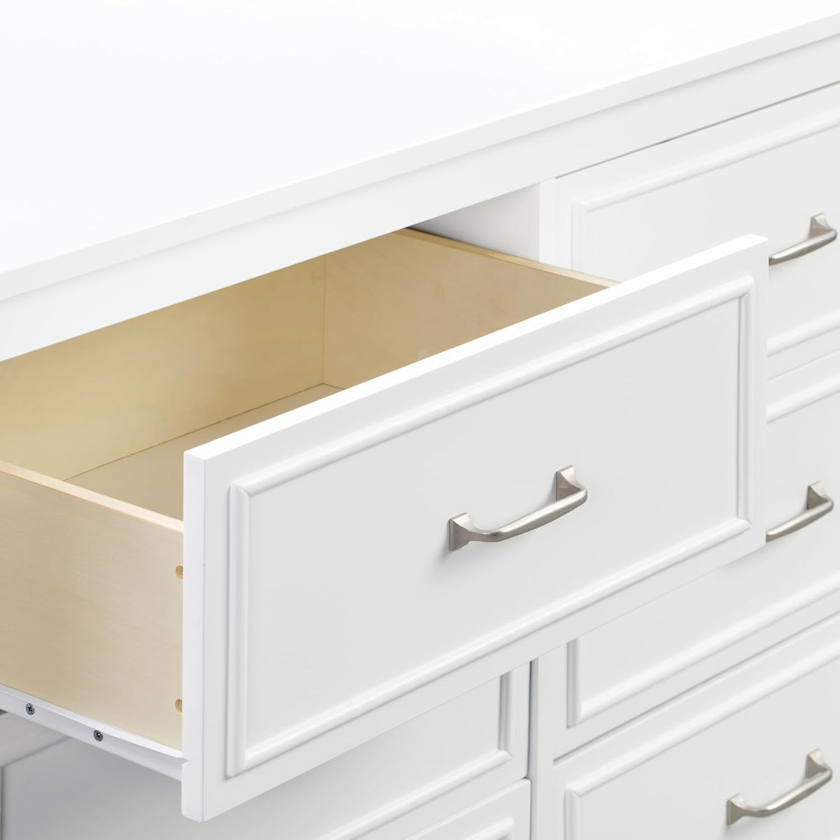 Close-up of an open top-left drawer showing light wood interior and a white drawer front with a brushed metal handle.