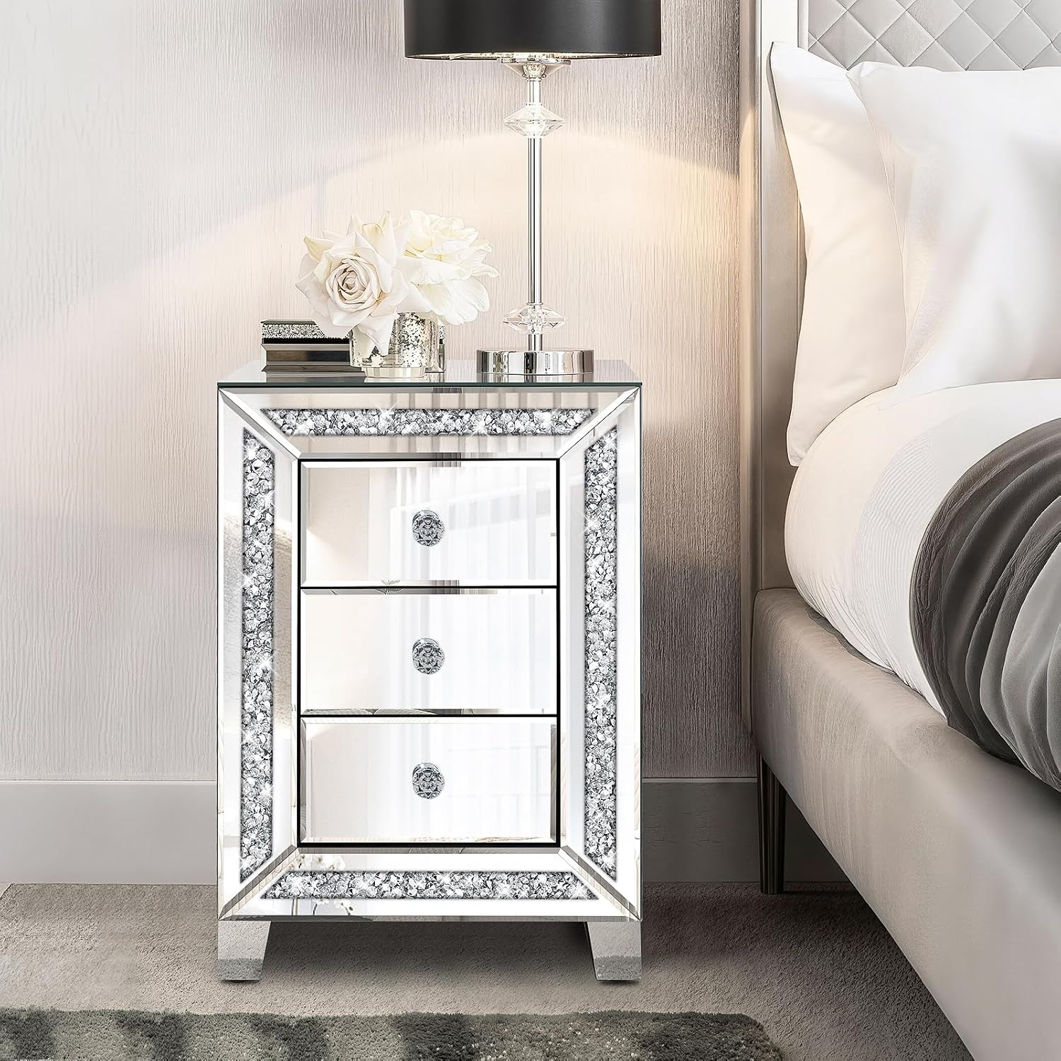 Front view of the mirrored nightstand styled at a bedside with a lamp and decorative flowers