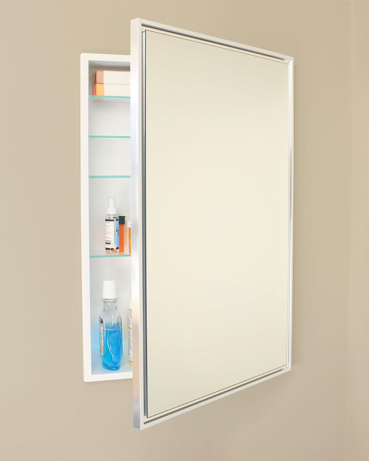 Silver-framed recessed mirror mounted on a beige wall with door slightly open showing glass shelves and bottles inside.
