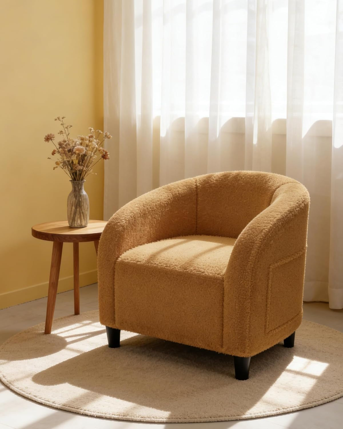 Beige boucle barrel chair on round rug beside a small wood side table and sheer-curtained window.