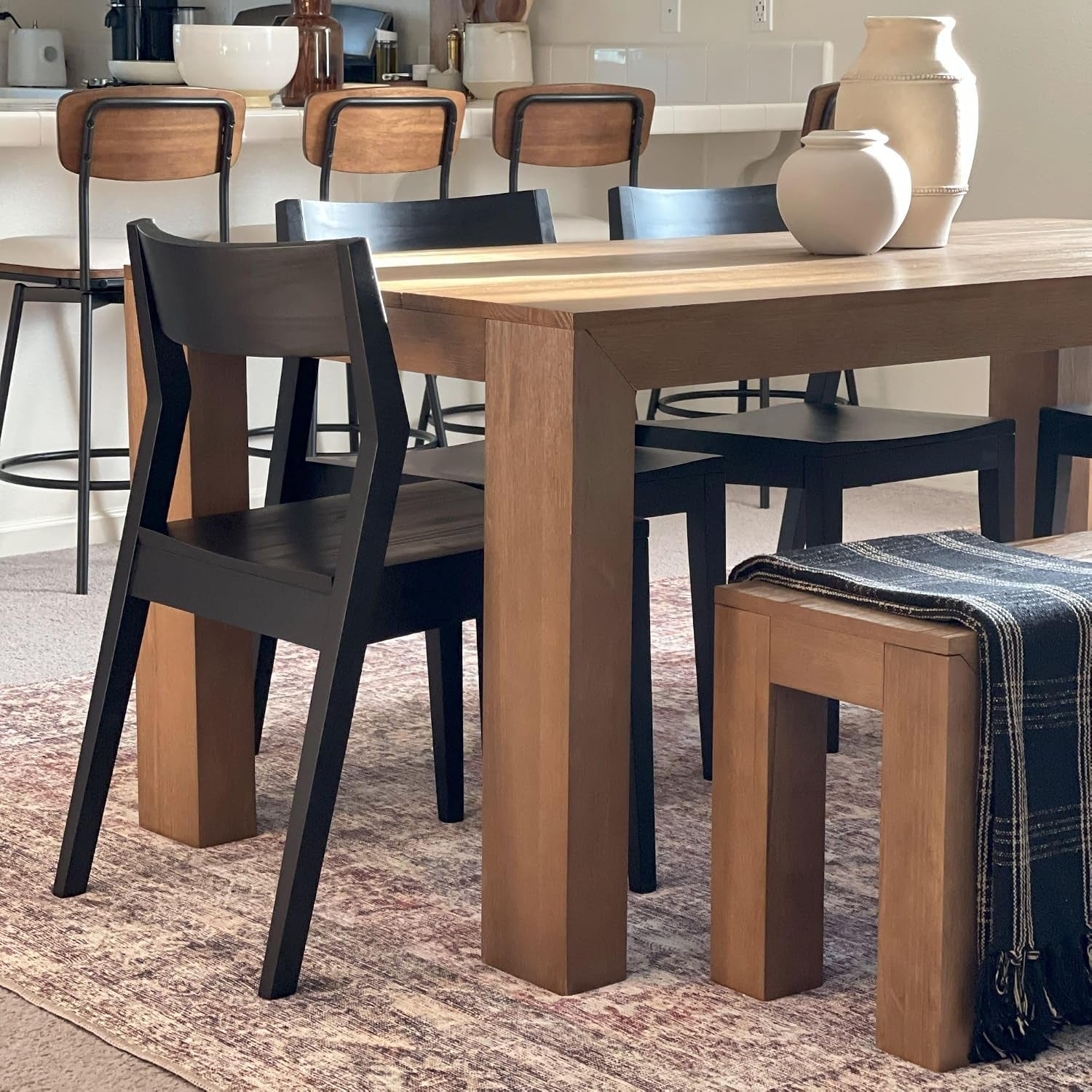 Dining room view with a solid pine table, thick square legs, black chairs and a wooden bench draped with a blanket.