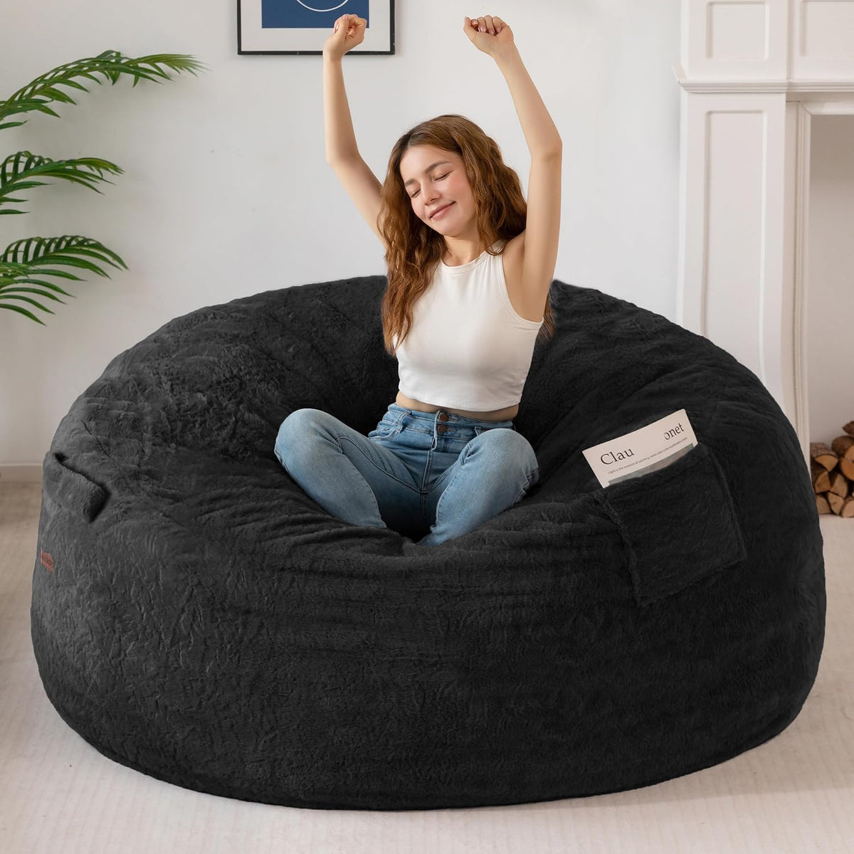 Angled view of the black bean bag with the model sitting cross-legged and stretching, showing deep, cushioned seat