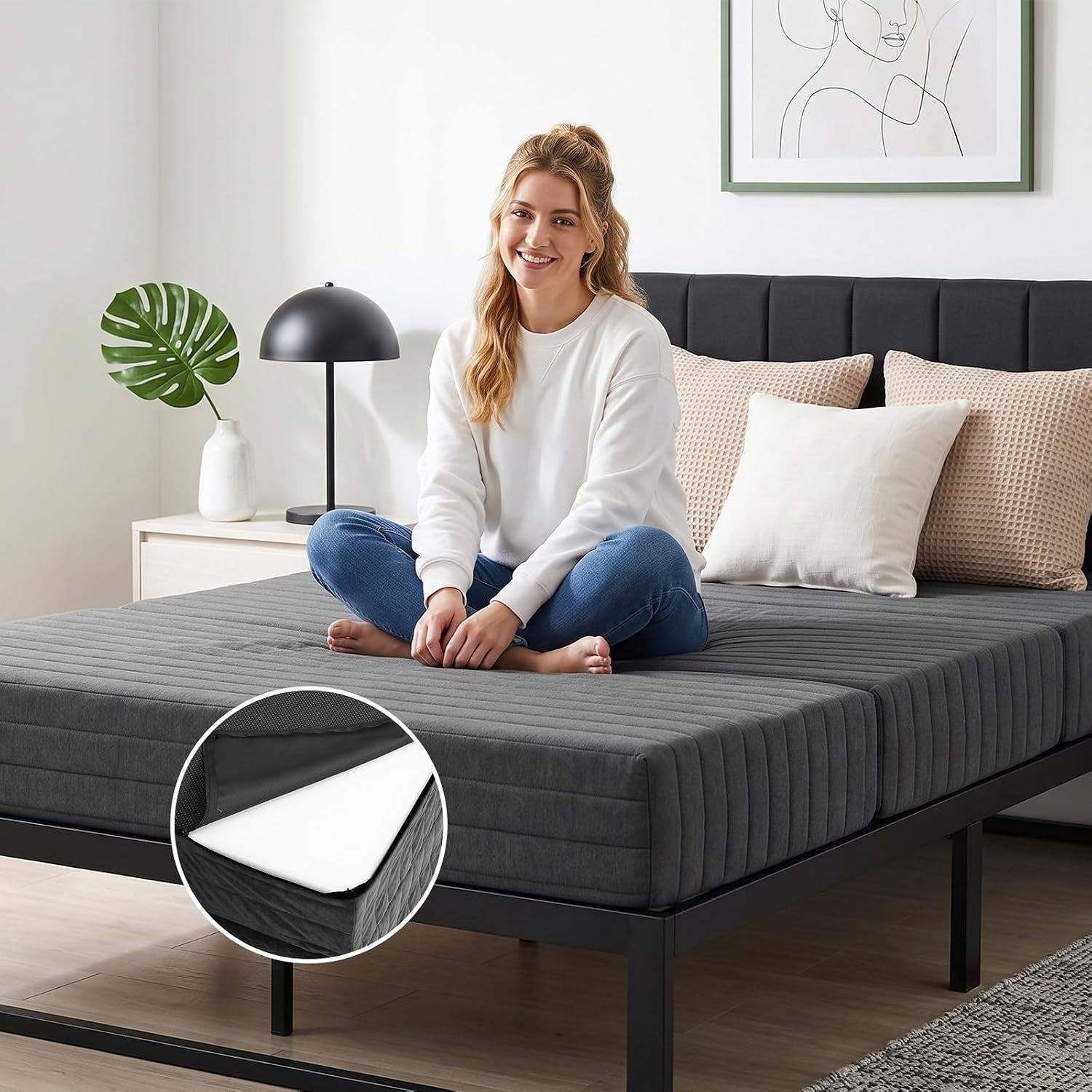 Woman sitting cross-legged on a dark gray trifold foam mattress on a metal bed frame, inset shows corner of foam under cover