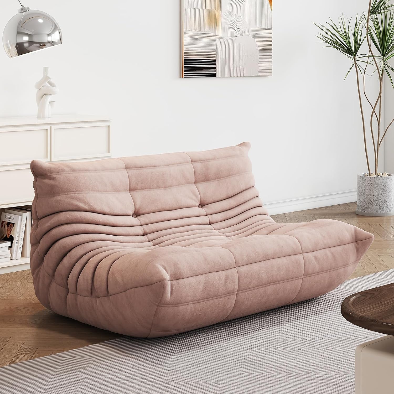 Blush‑pink two‑seat lounge sofa shown in a bright living room with rug and wall art.