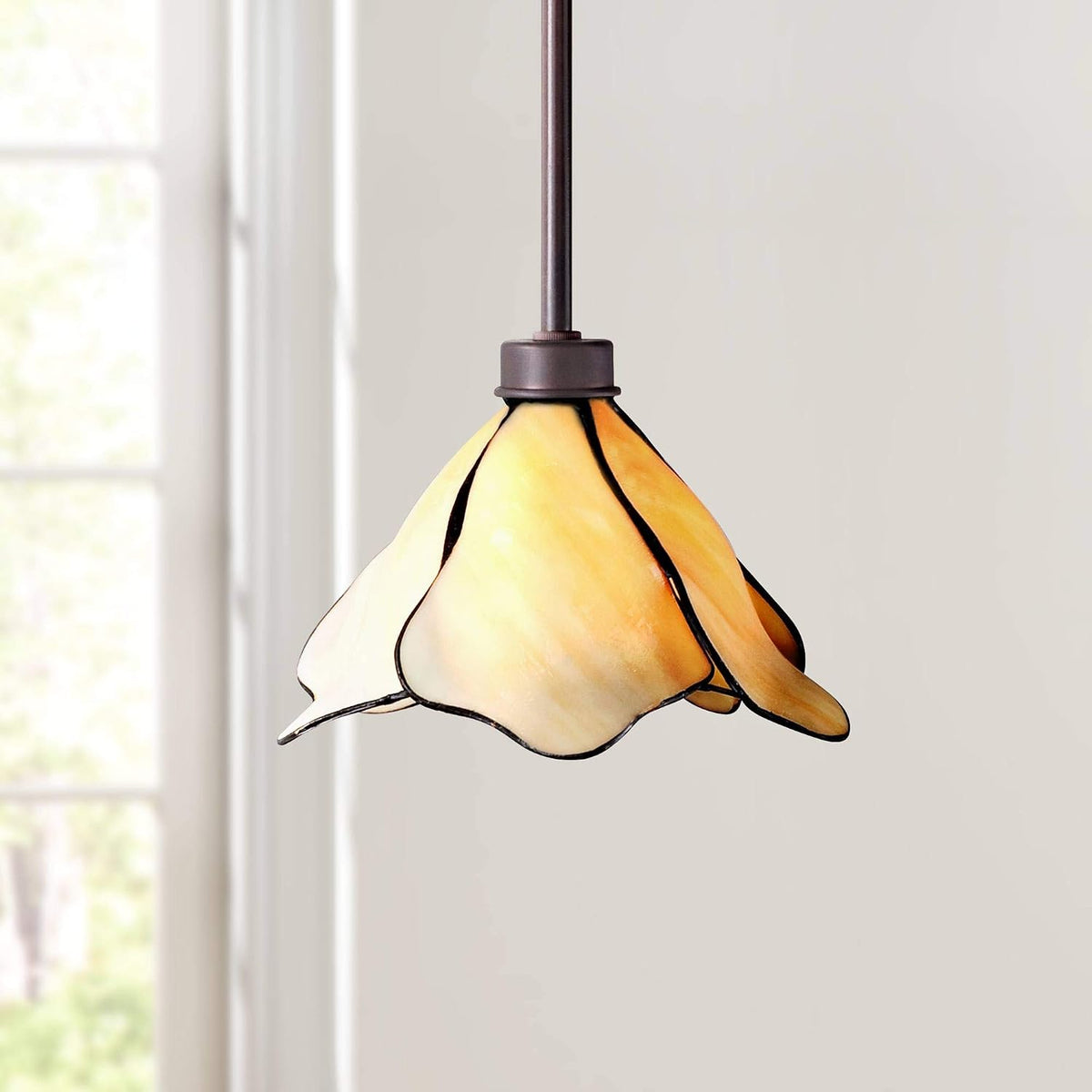 Amber petal-shaped Tiffany-style glass pendant shown lit, angled front view near a window.