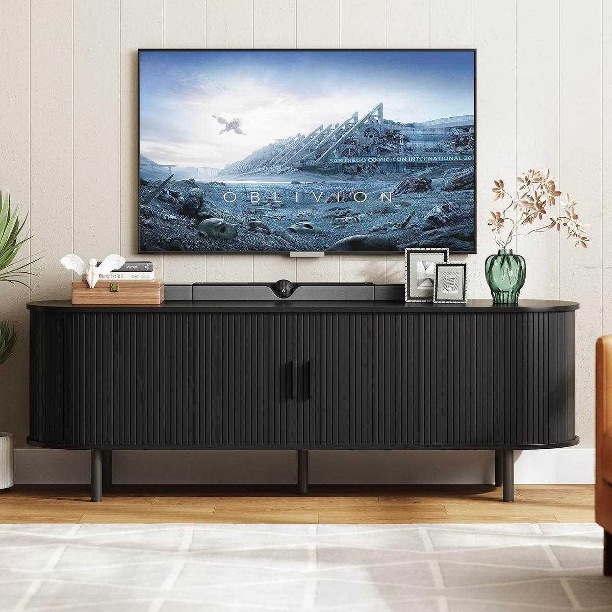 Front view of black TV stand with rounded fluted doors, tabletop decor and a wall-mounted TV above.