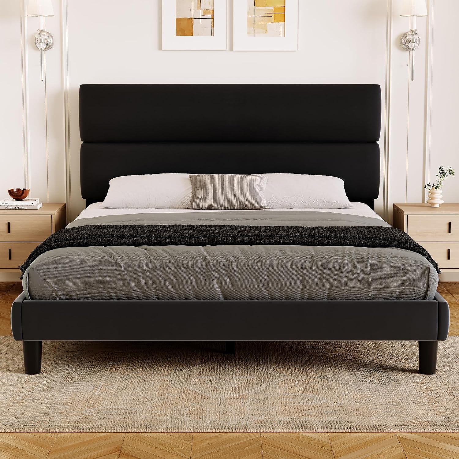 Symmetrical bedroom view of a wide black bed with an upholstered frame and two-part headboard.