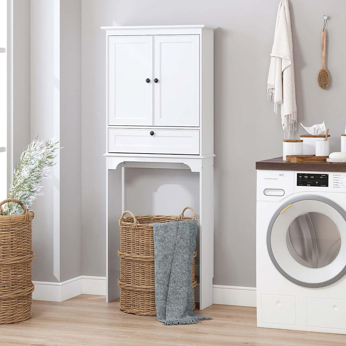 White slim storage cabinet in a laundry or bathroom corner, freestanding with inset doors and a single drawer front