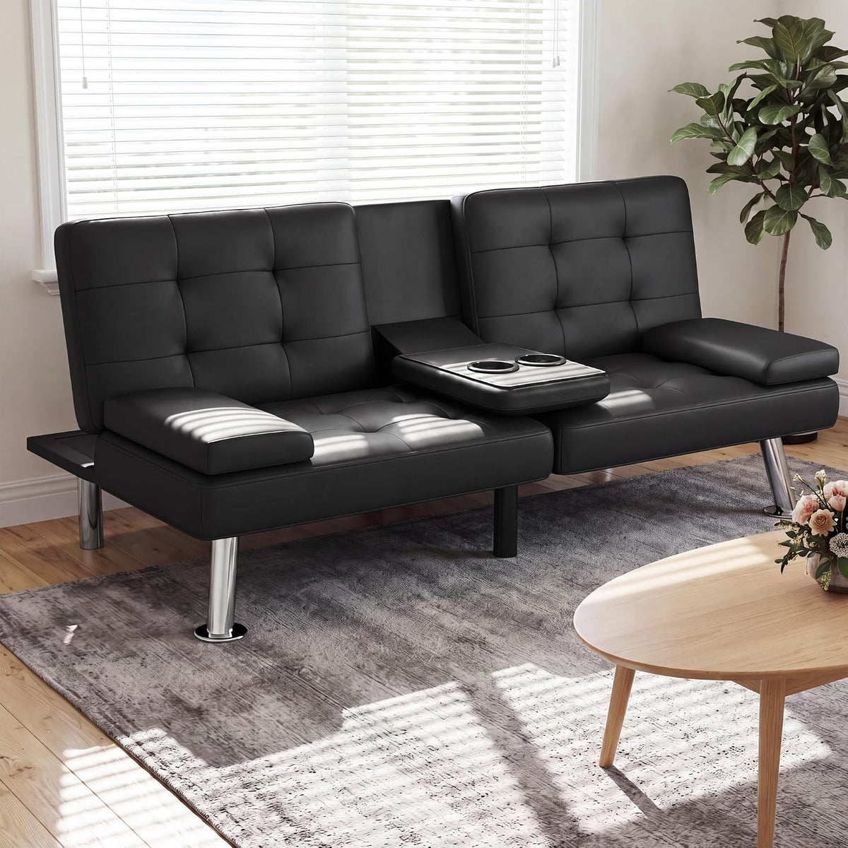 Studio-style view of black faux-leather futon sofa bed with metal legs and folded armrests, cup holder visible.