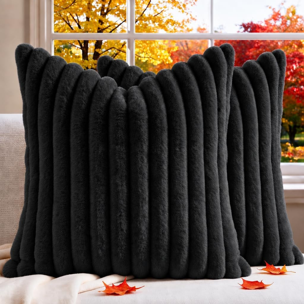 Two dark charcoal ribbed faux-fur square pillow covers on a light sofa with autumn trees outside the window.