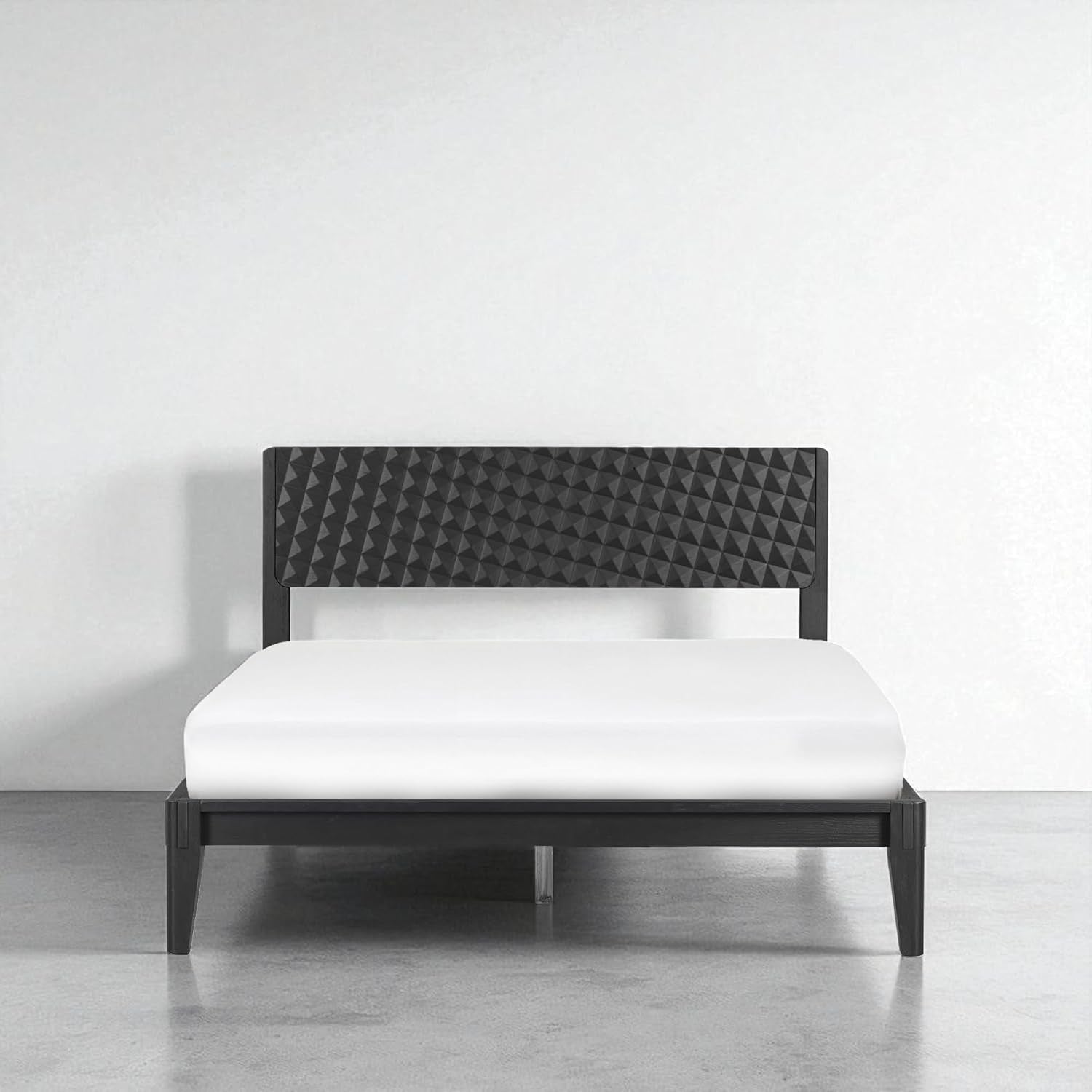 Frontal studio view of the bed frame against a white wall showing the geometric headboard and low-profile frame.