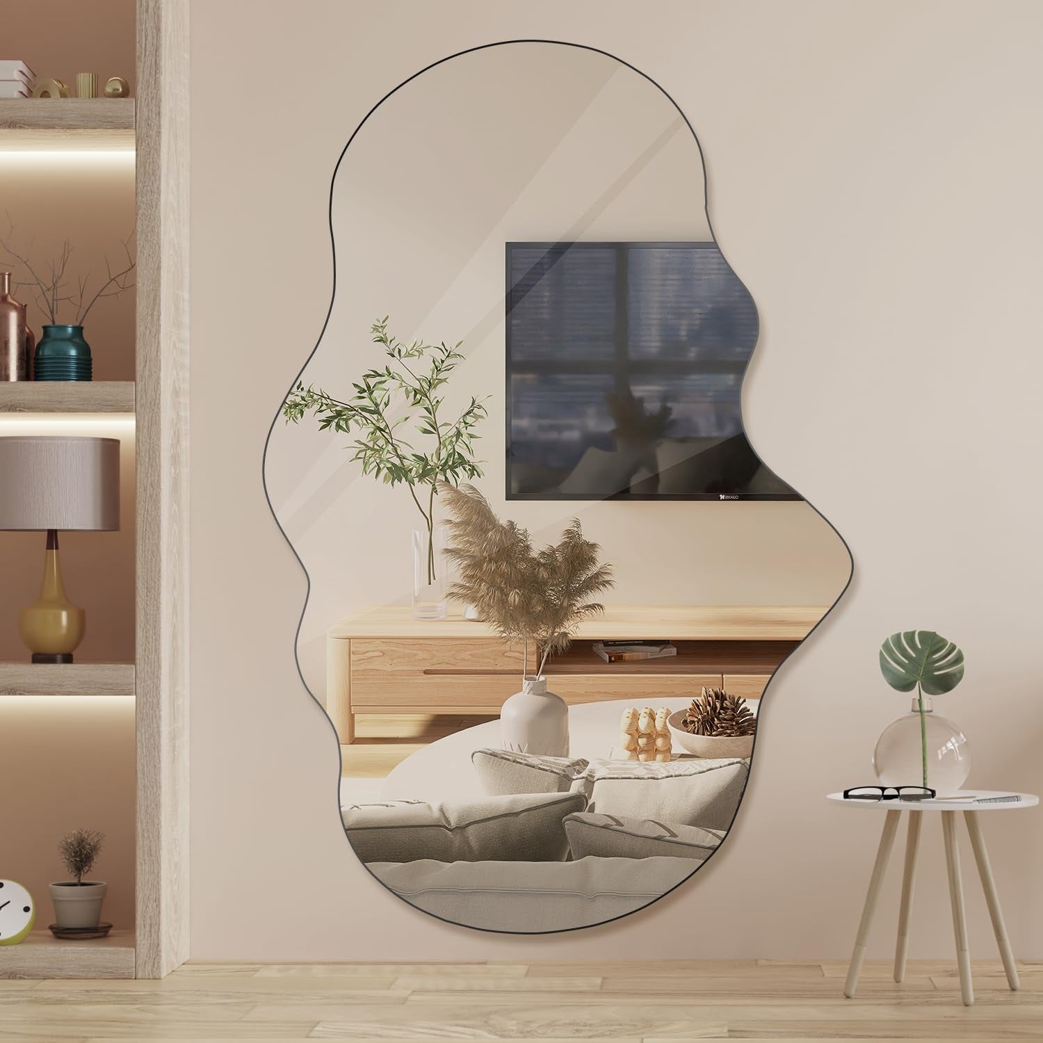 Tall cloud-shaped mirror with thin black edge reflecting a TV, wooden media console and pampas grass vase.