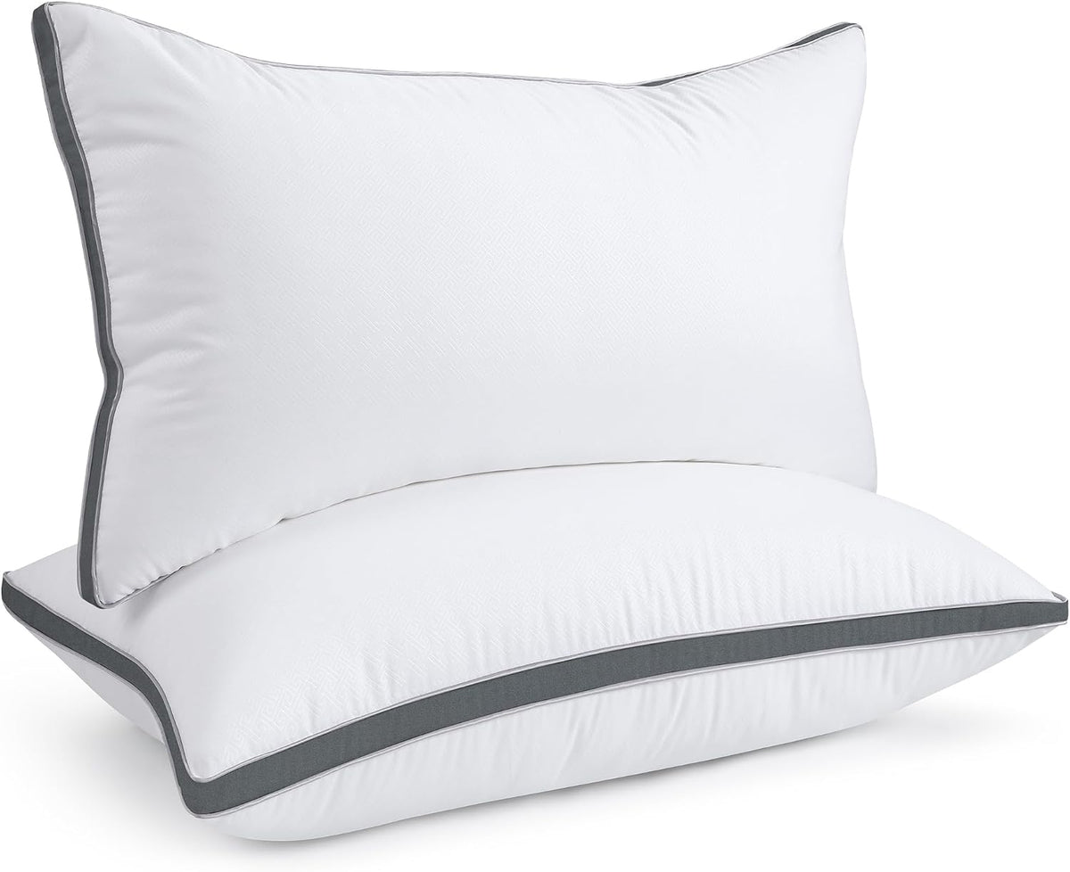 Two white pillows stacked at an angle with contrasting dark-gray piping along the edges.