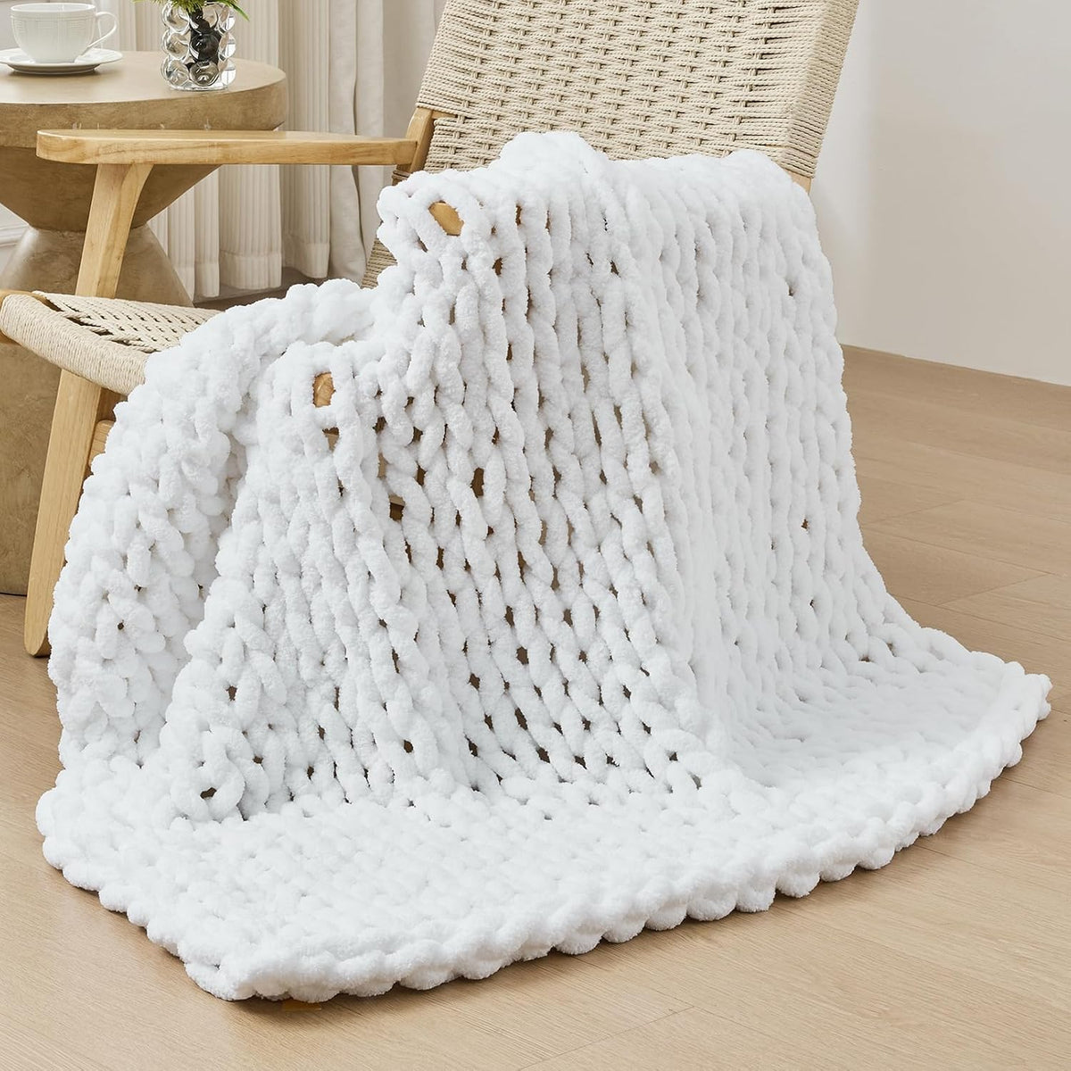Chunky knit throw draped over a woven wooden chair, pooling onto a light wood floor.