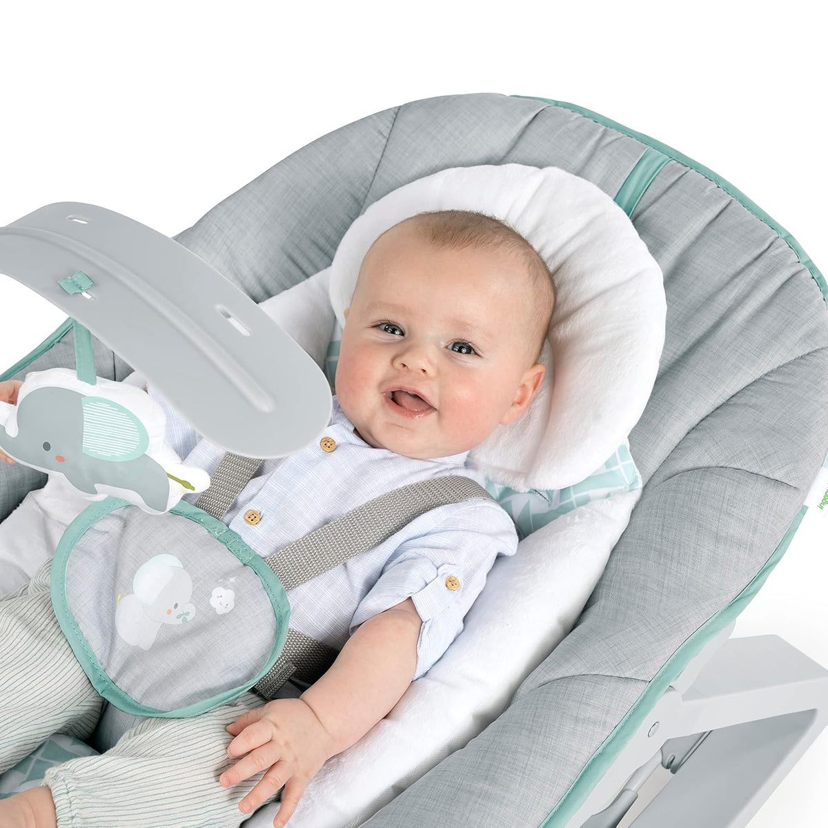 Smiling baby reclined in the padded bouncer under a toy bar with a hanging elephant.