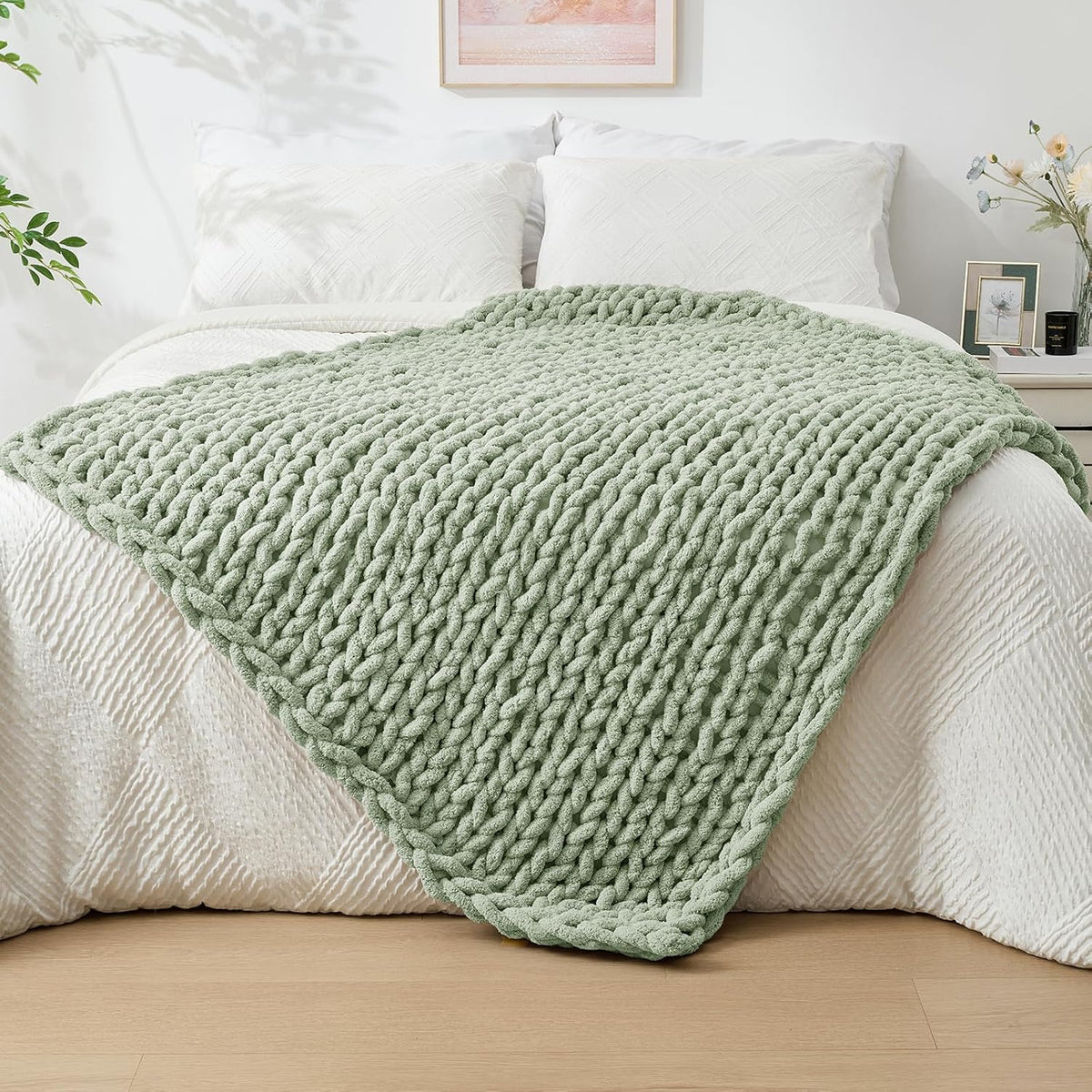 Sage-green chunky knit throw spread diagonally over a white quilted bed.
