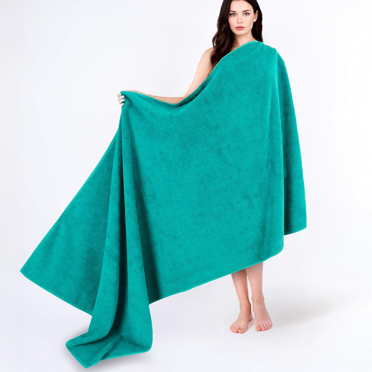 Model on a white background holding a large teal bath towel draped to show its full size.