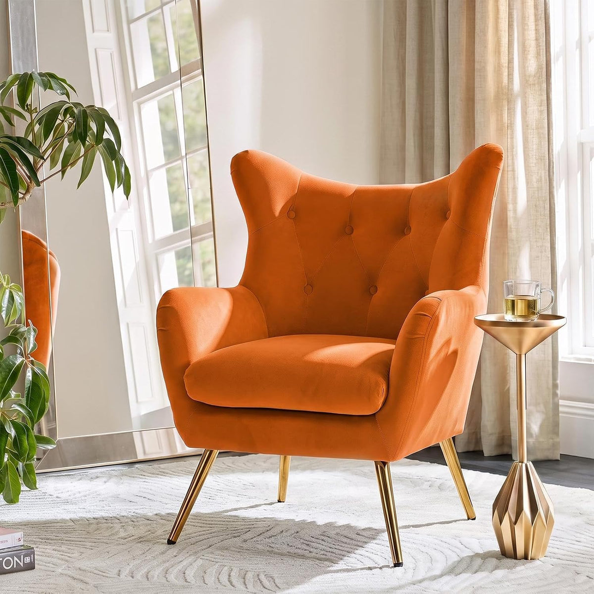 Cropped detail of an orange velvet wingback chair showing tufted back, armrest and gold leg.
