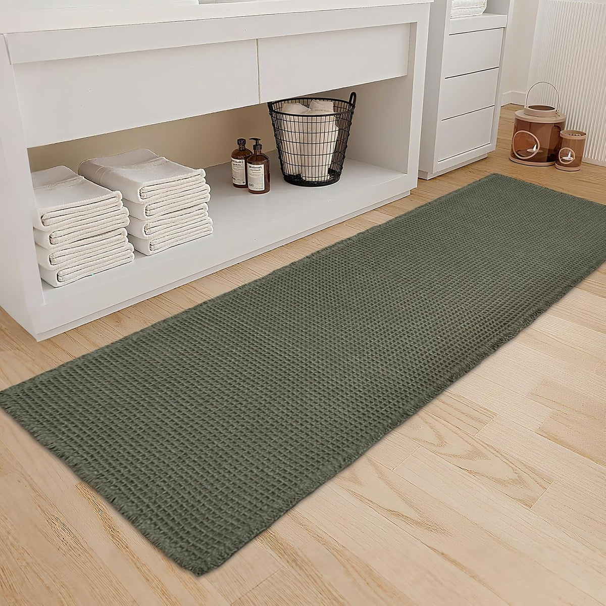 Long olive-green waffle bath mat laid in front of a white vanity on light wood floor