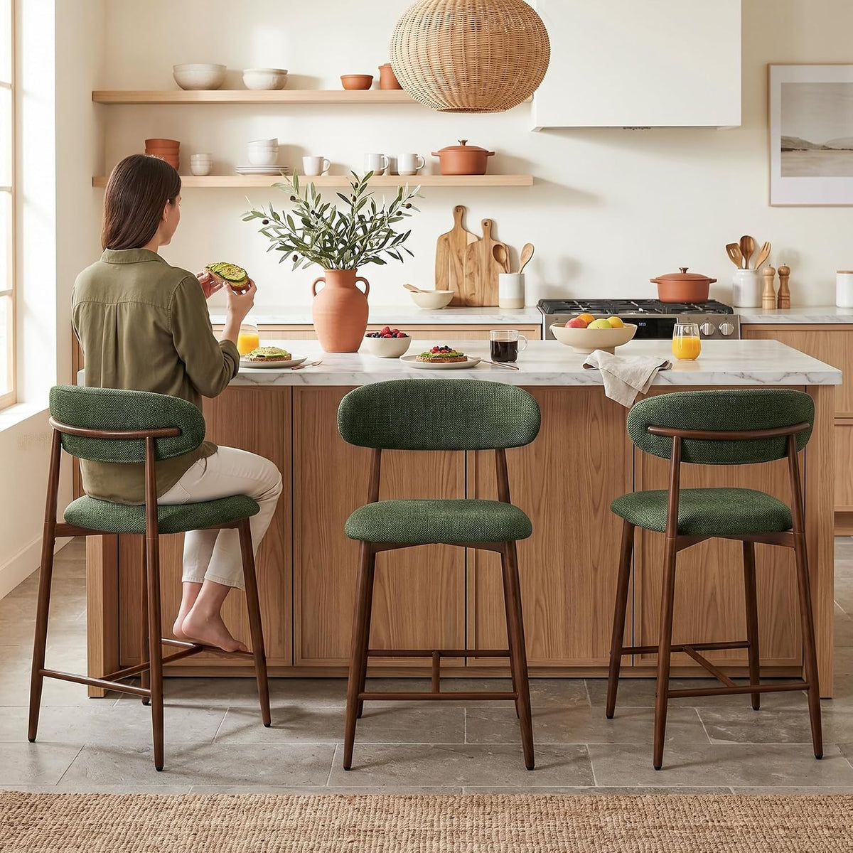 Three green upholstered counter stools lined at an island, one occupied by a person eating.