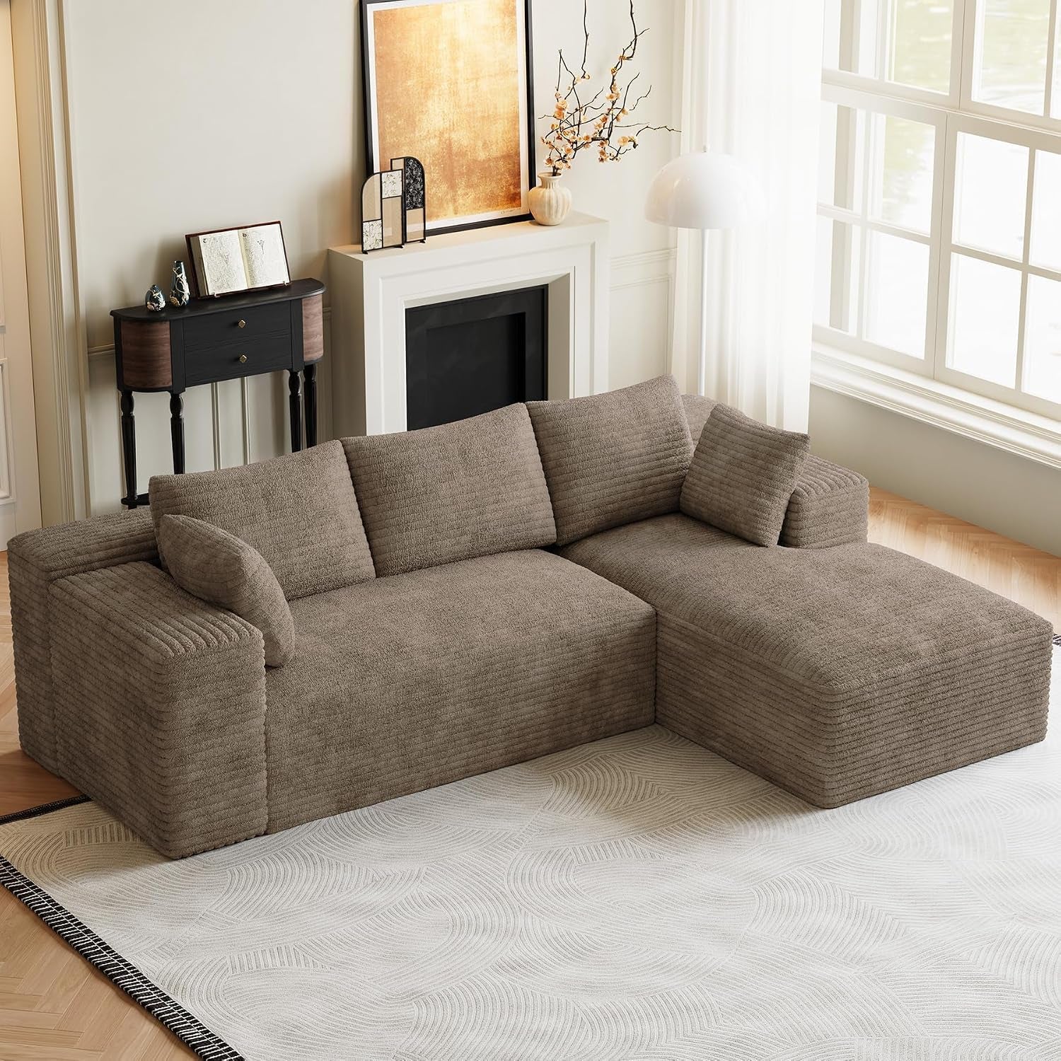Taupe-colored L-shaped sectional with chaise shown in a softly lit room with rug and fireplace.