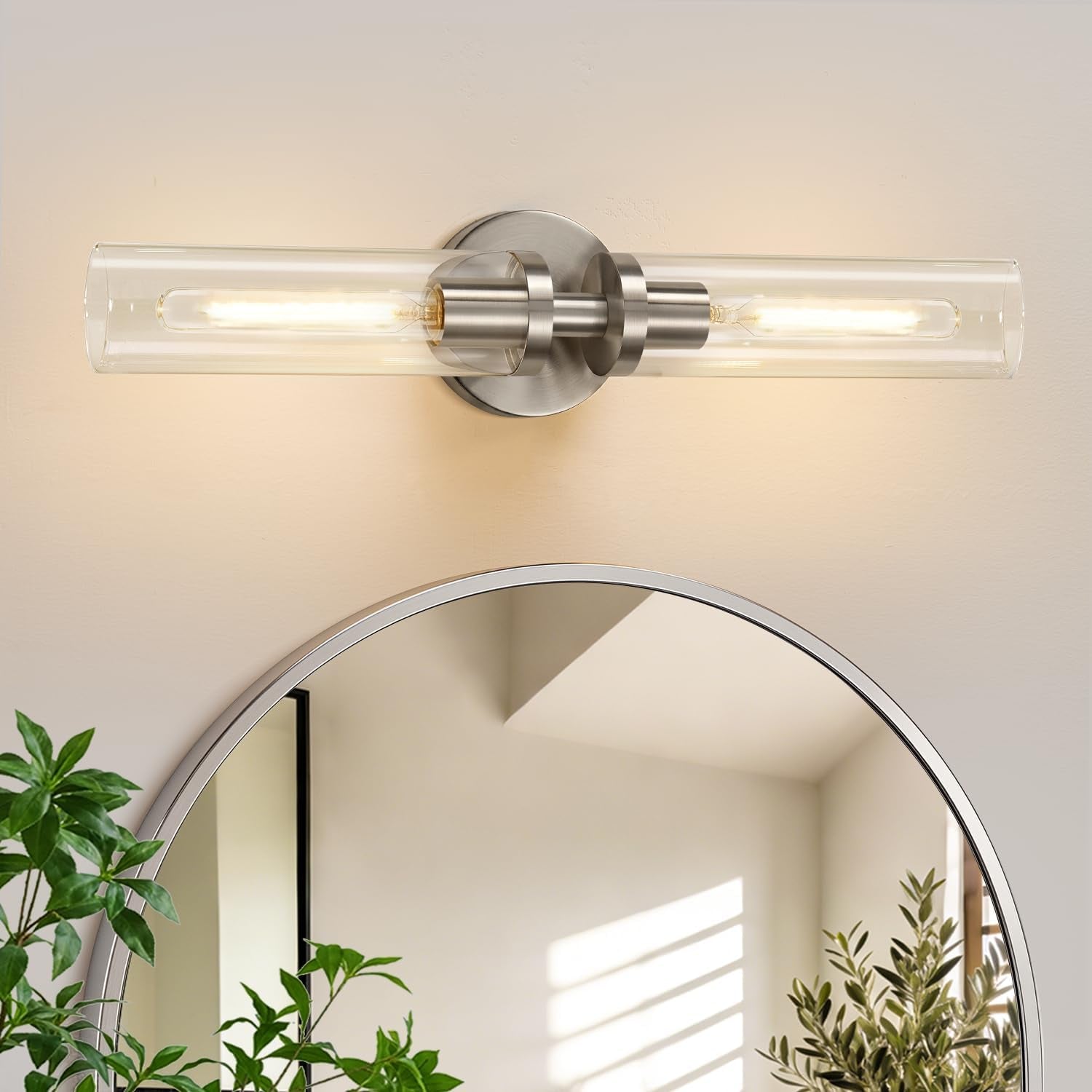 Single horizontal wall sconce in brushed silver finish above a round mirror and plants.