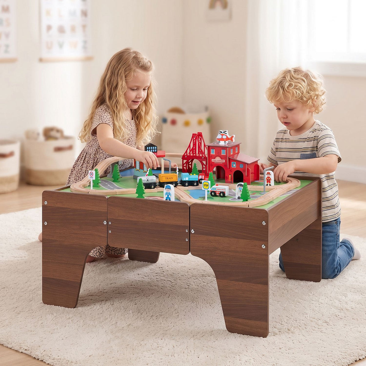 Two children play with toy trains on a wooden train table in a bright room.