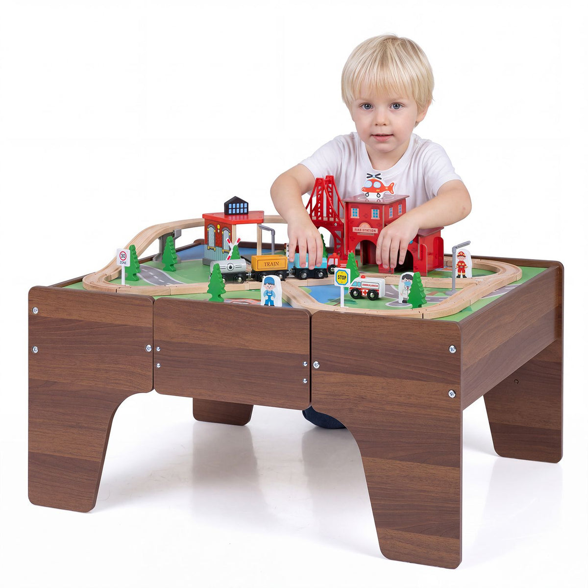 A child reaches across the train layout on a low wooden table against a white background.