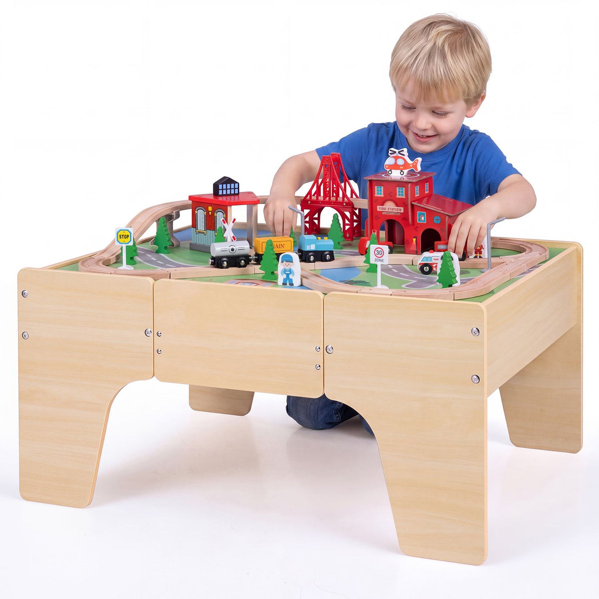 A child plays with toy trains on a wooden table against a white background.