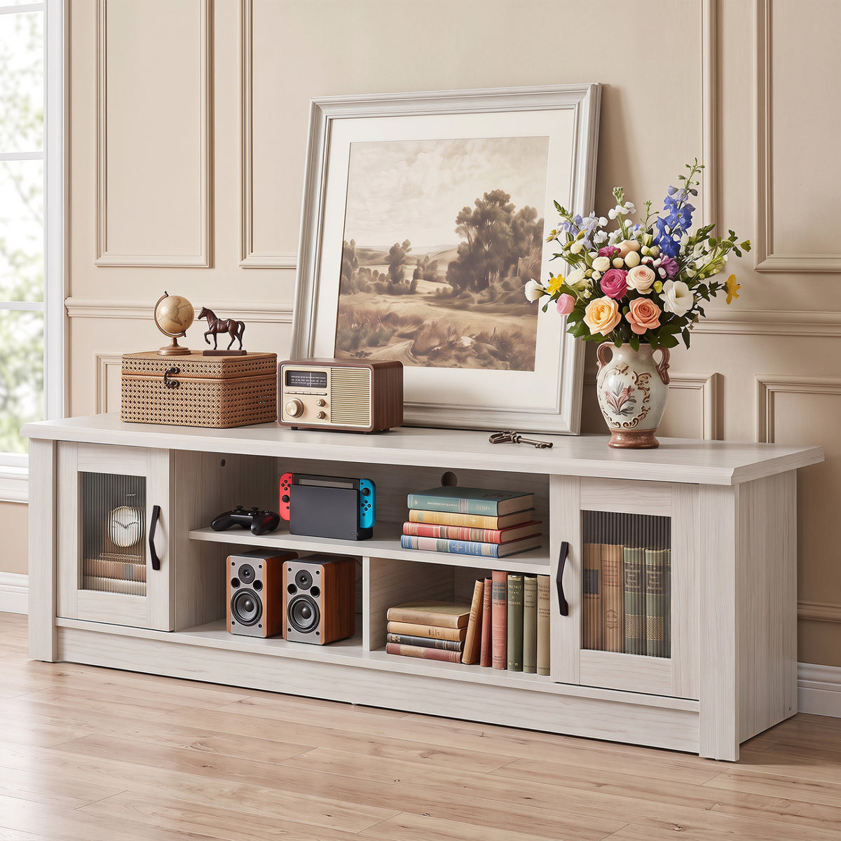 White TV stand styled with books, speakers, a game console, framed art, and flowers.