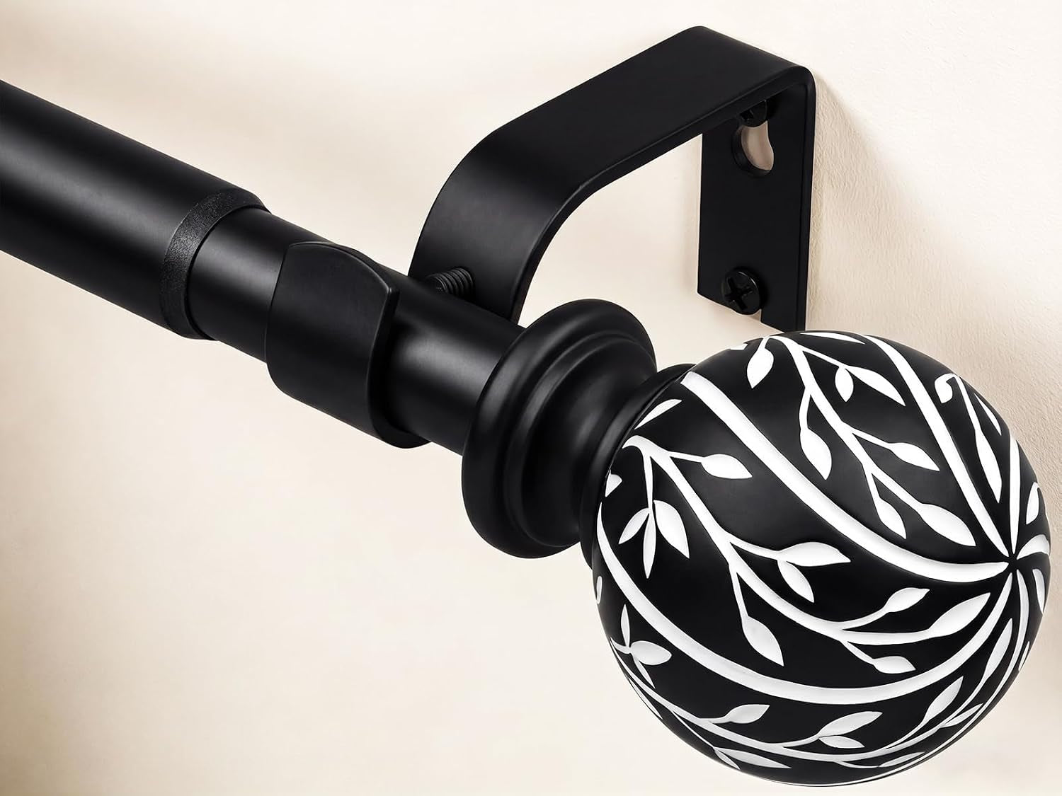 Detail of matte black rod with squared wall bracket and contrasting white-leaf patterned spherical finial.
