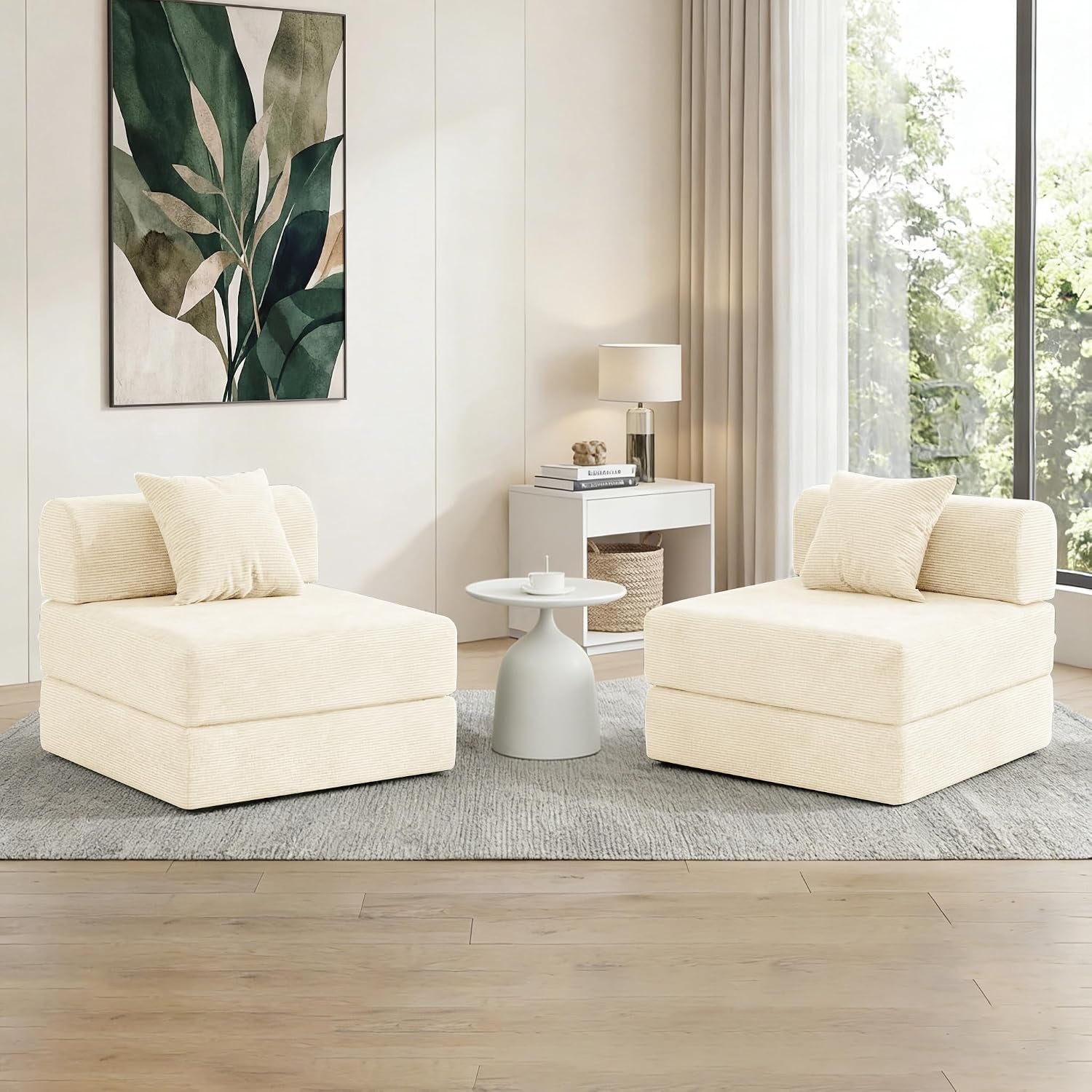 Two cream corduroy armless chairs facing each other with a small round table between them in a bright room.