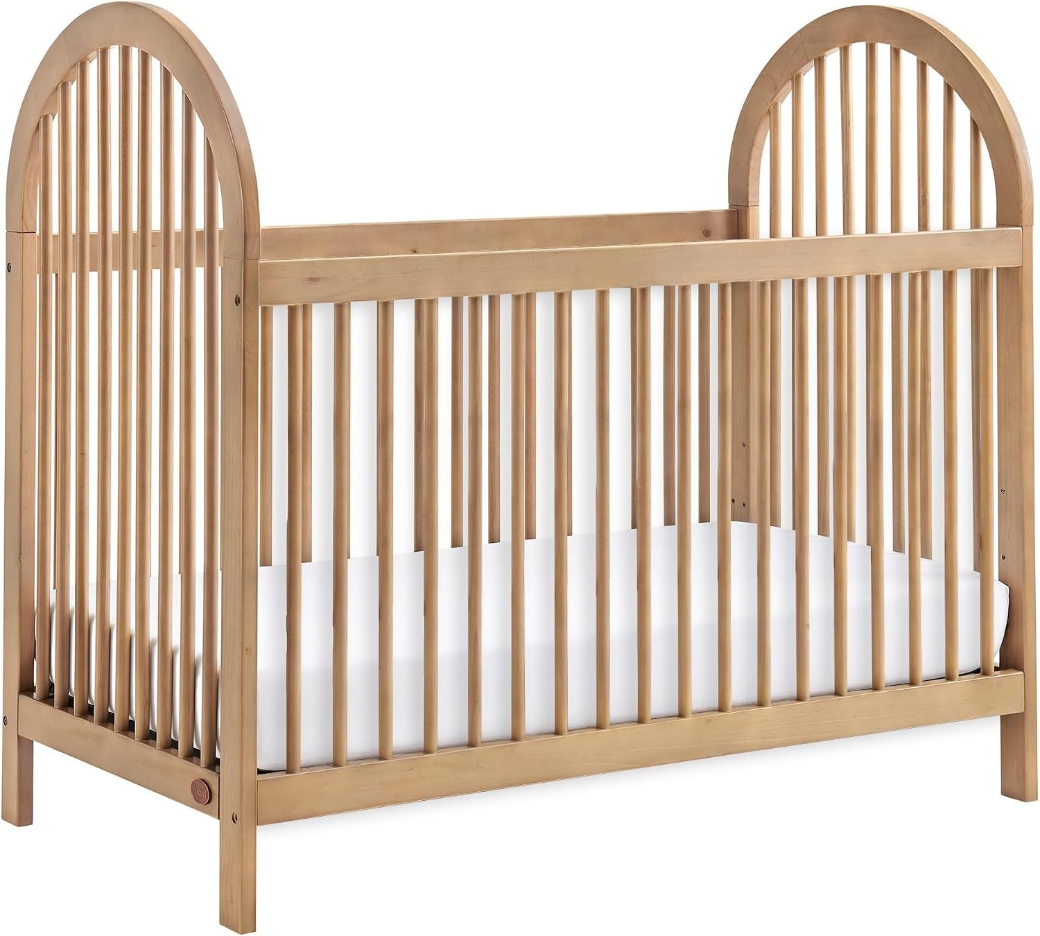Honey-toned wooden convertible crib with arched end panels and vertical slats, mattress inside