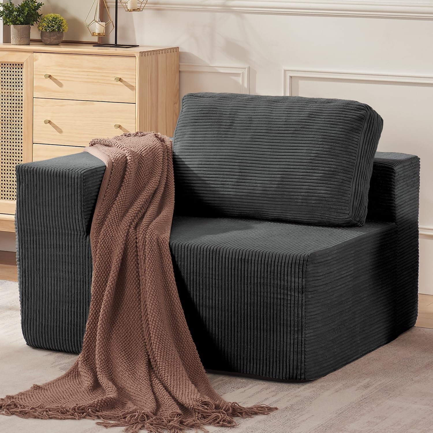 Close side view of a single black modular sofa module with ribbed fabric, wide arm, back cushion and a draped brown knit