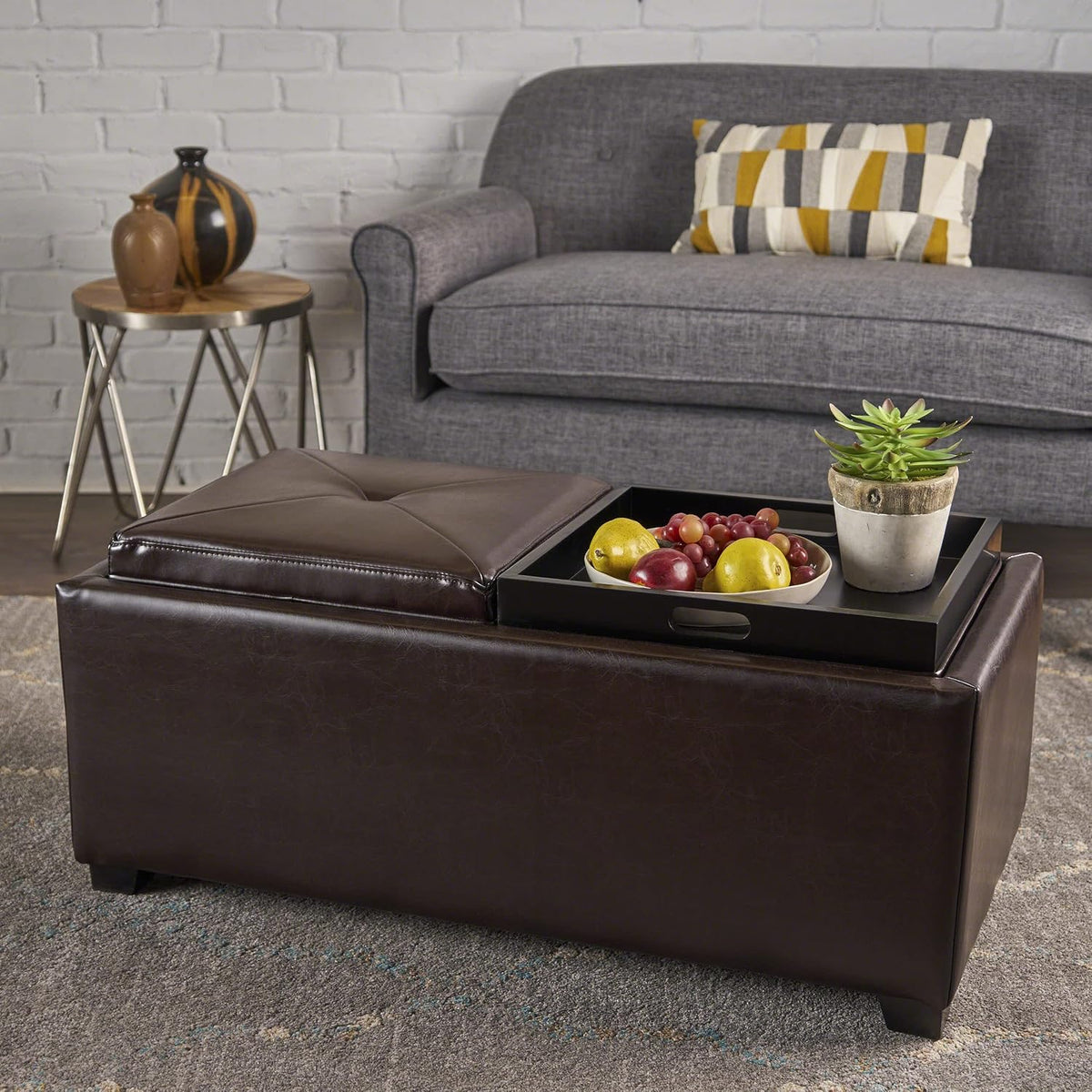 Tray on the ottoman holds a bowl of fruit and a small potted succulent beside a closed tufted cushion.