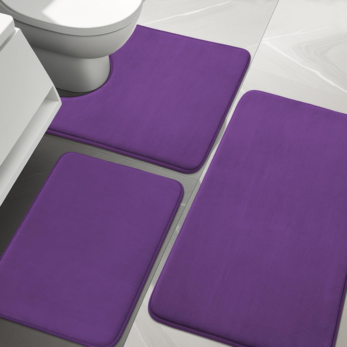 Top-down bathroom view showing three purple memory-foam rugs, one contoured around a toilet base.