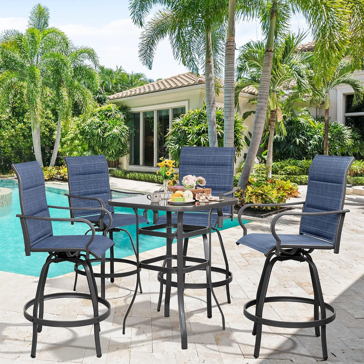 Sunlit scene of four blue swivel bar chairs around the glass table with palm trees and pool behind.